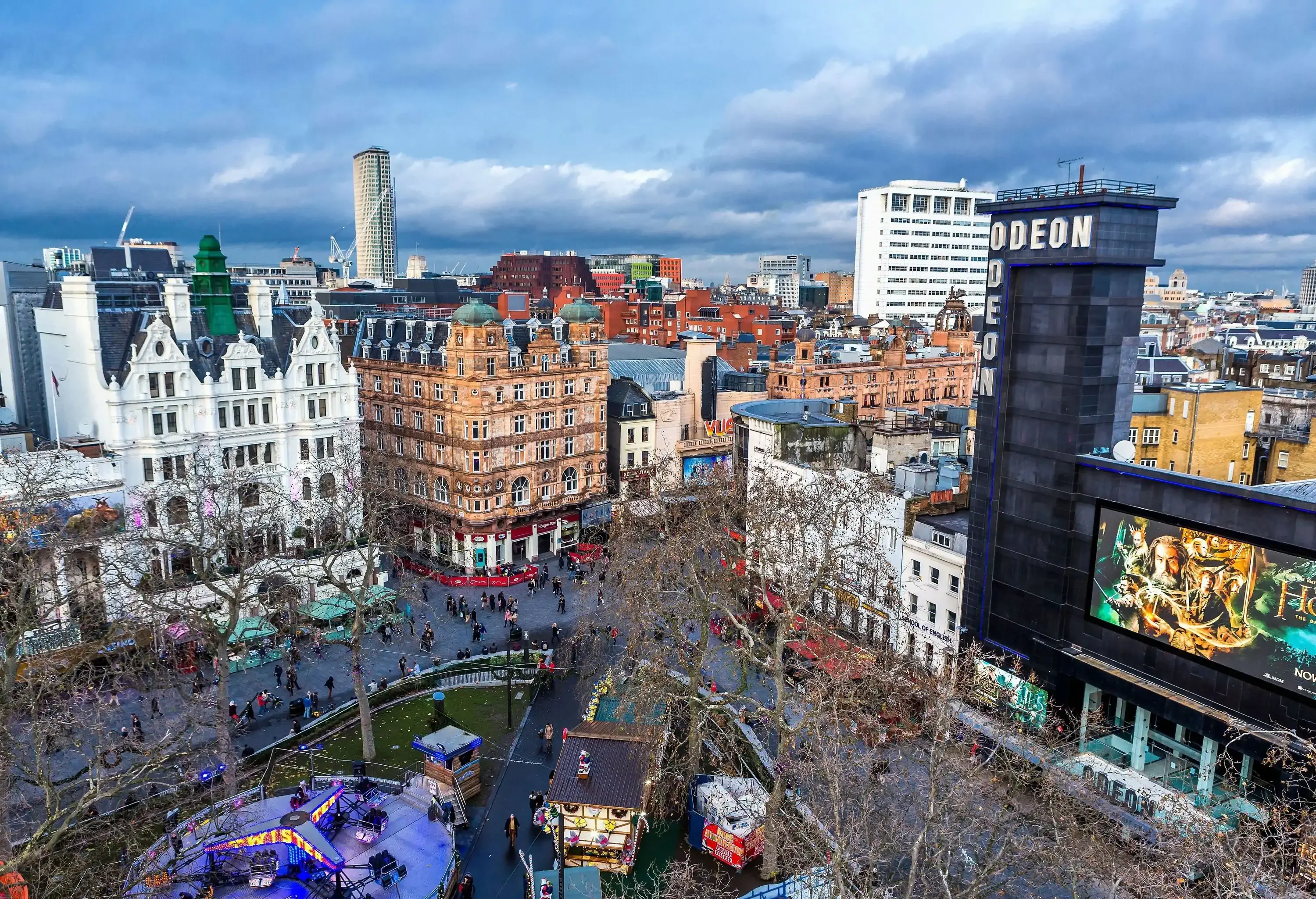 Aerial view of Leicester Square in London, UK, with central stalls surrounded by bare trees and a mix of modern and vintage building structures.