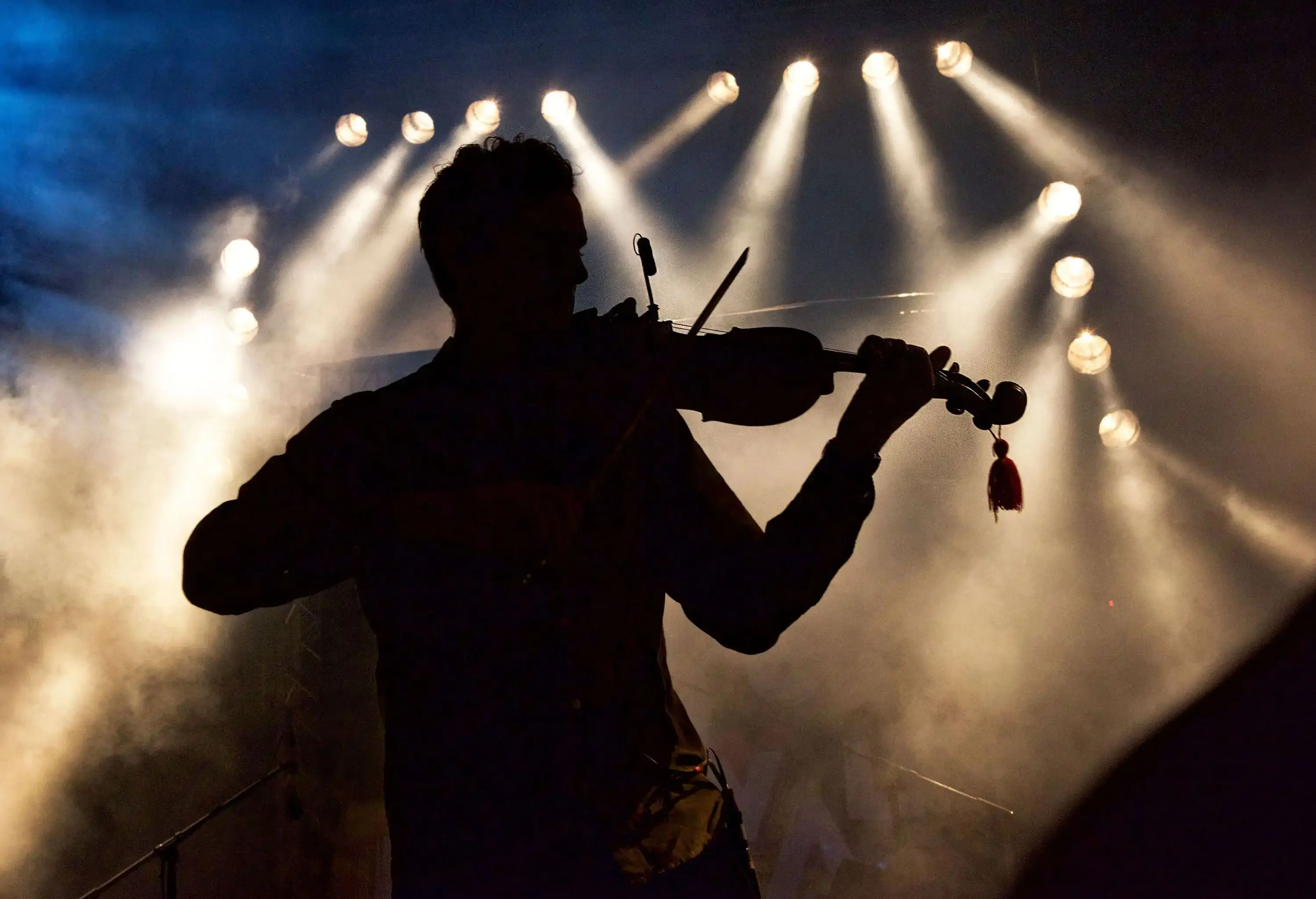 A striking silhouette of a person playing a violin is illuminated against a backdrop of vibrant, colourful lights.