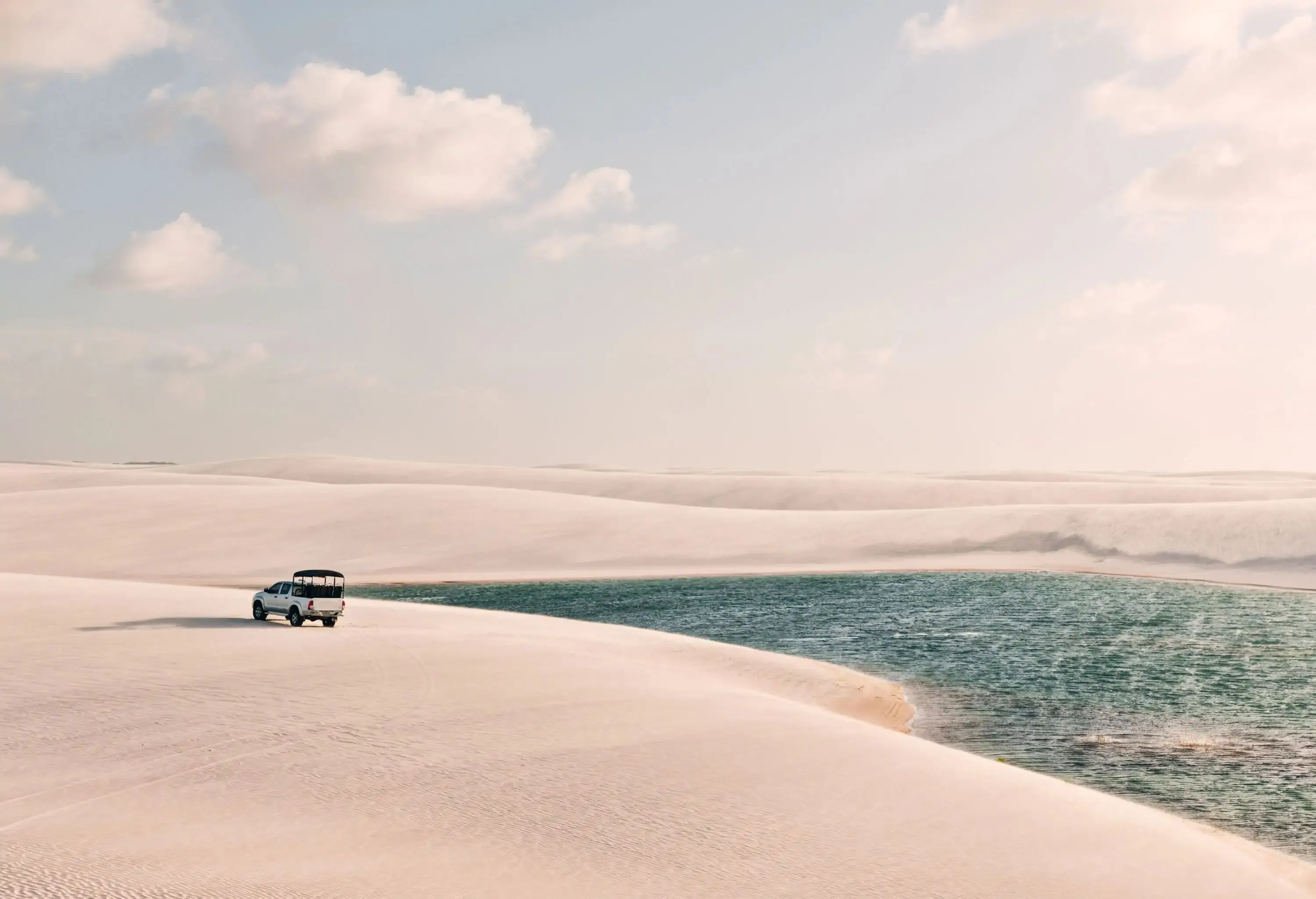 A car parked on the expansive white sand dunes by the river.