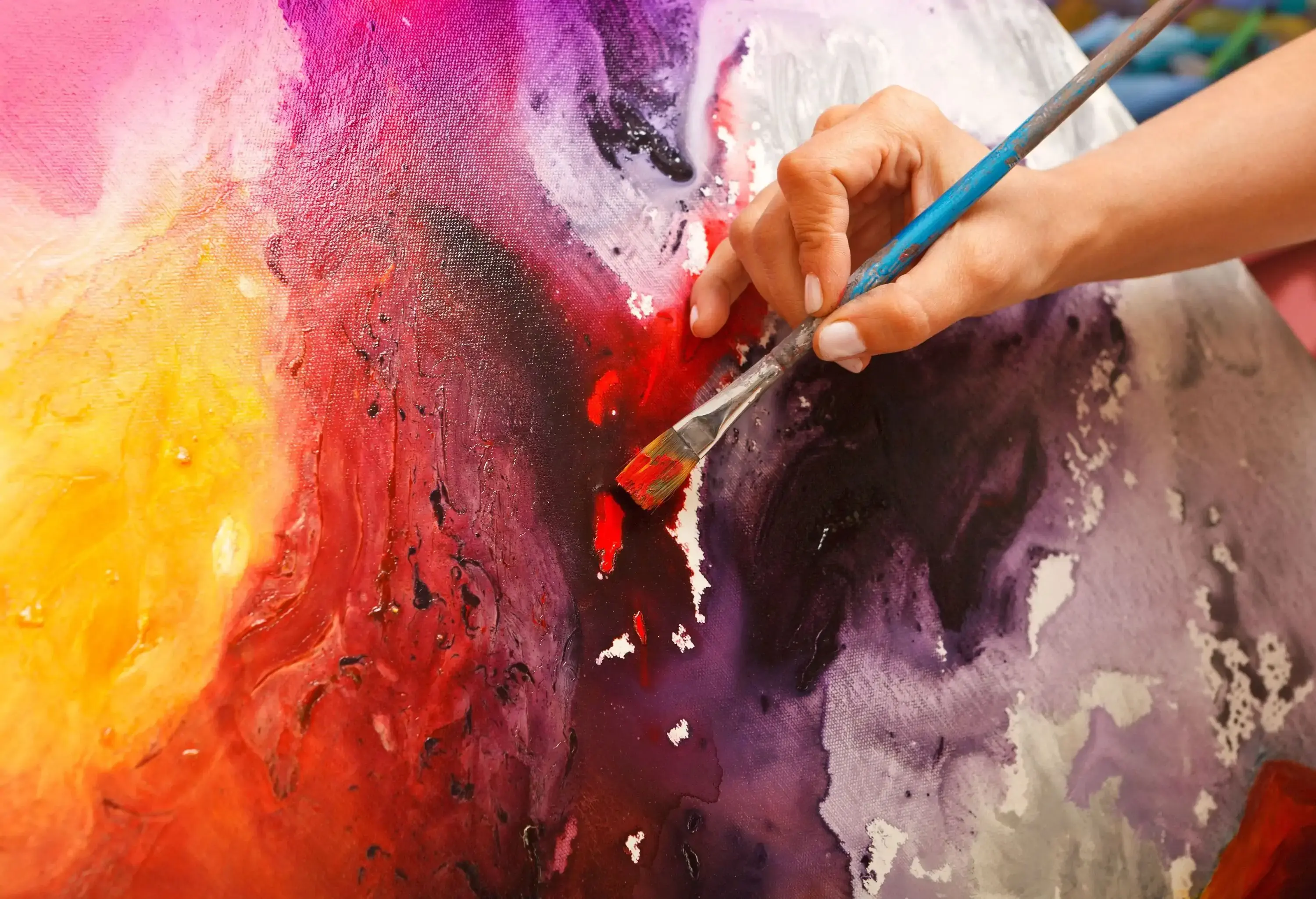 A painter brushing red paint on a canvas with splashes of other hues.