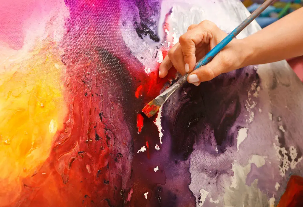 A painter brushing red paint on a canvas with splashes of other hues.
