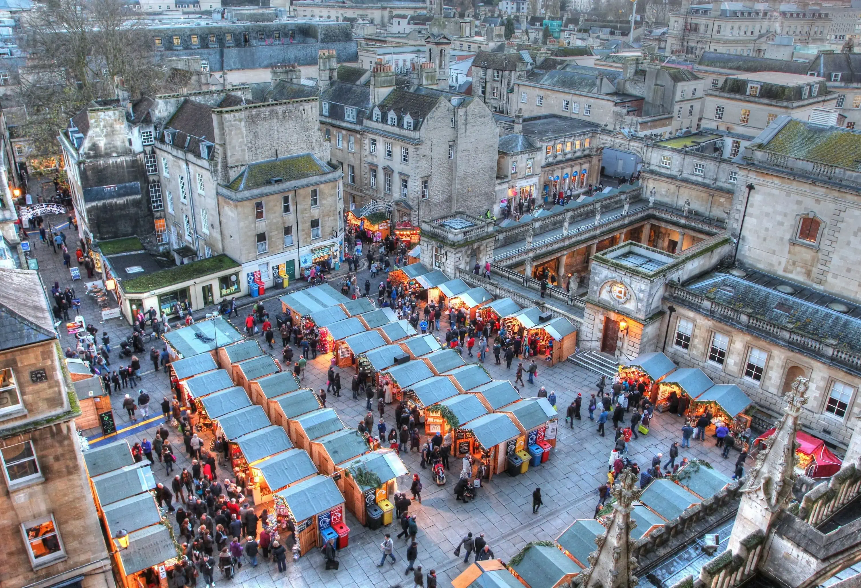 People around the shops in tents in an open cobbled space for a holiday market.