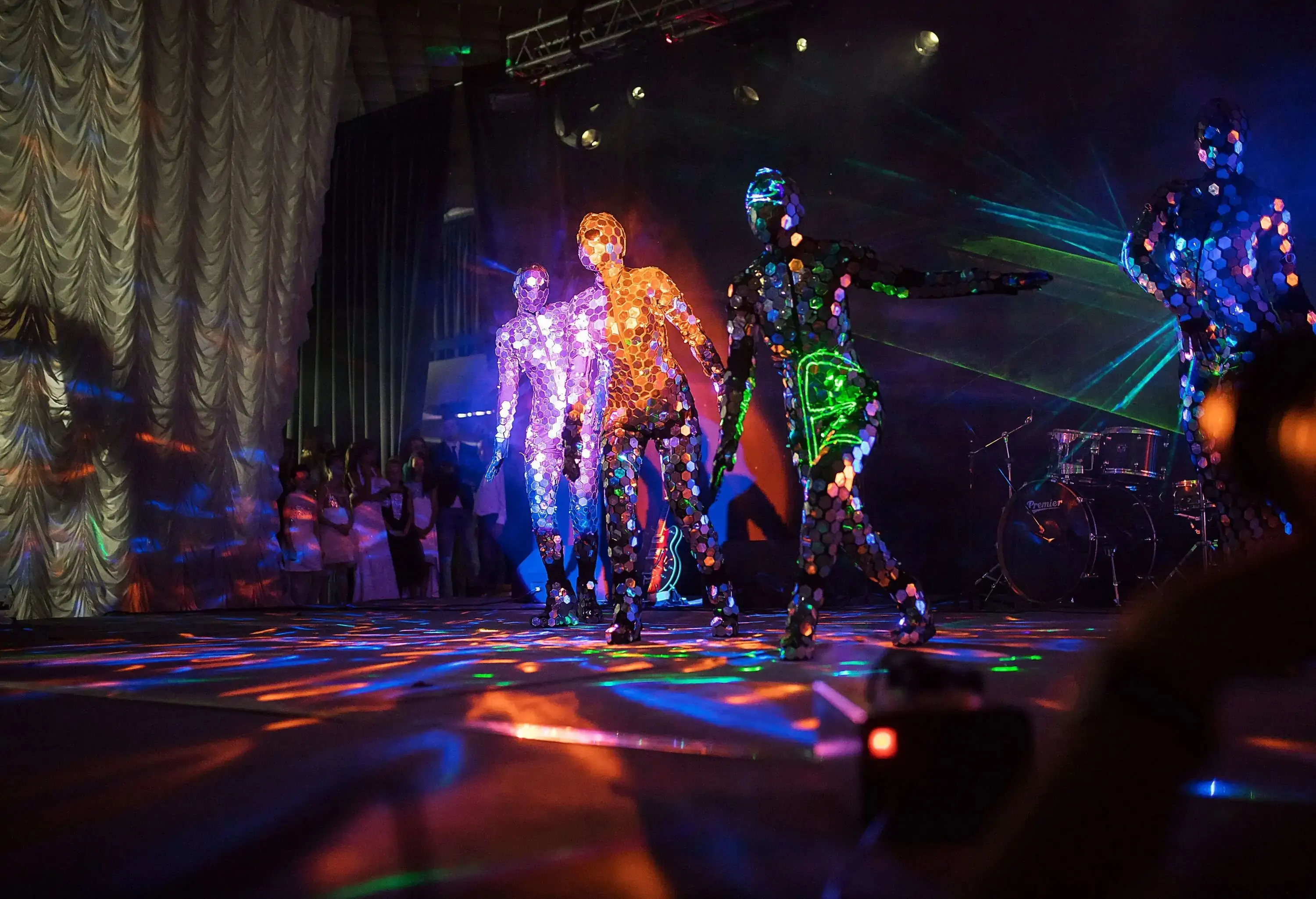 Performers wearing mirror suits dance on the stage during a dazzling light show.