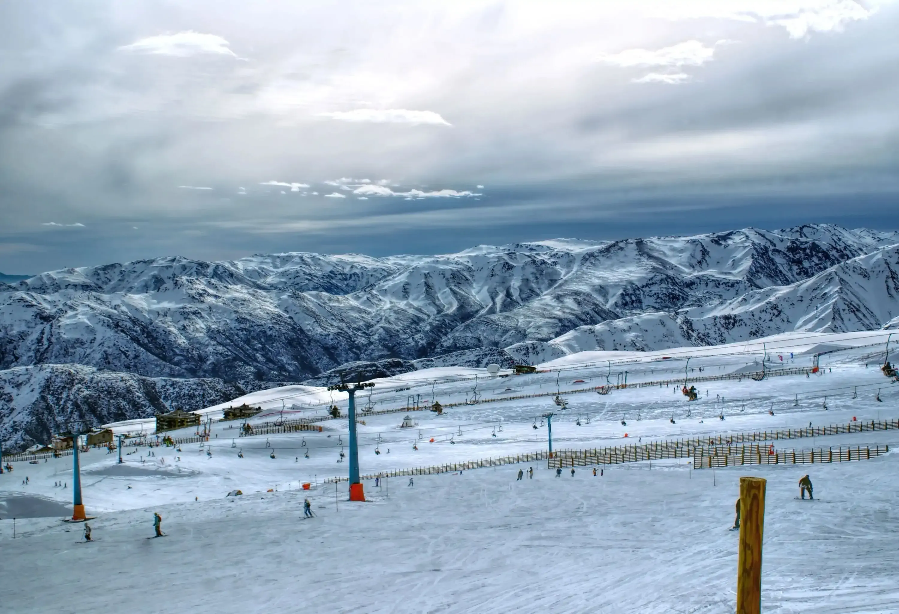 A wide ski area with aerial lifts overhead and a stunning mountain range in the background.