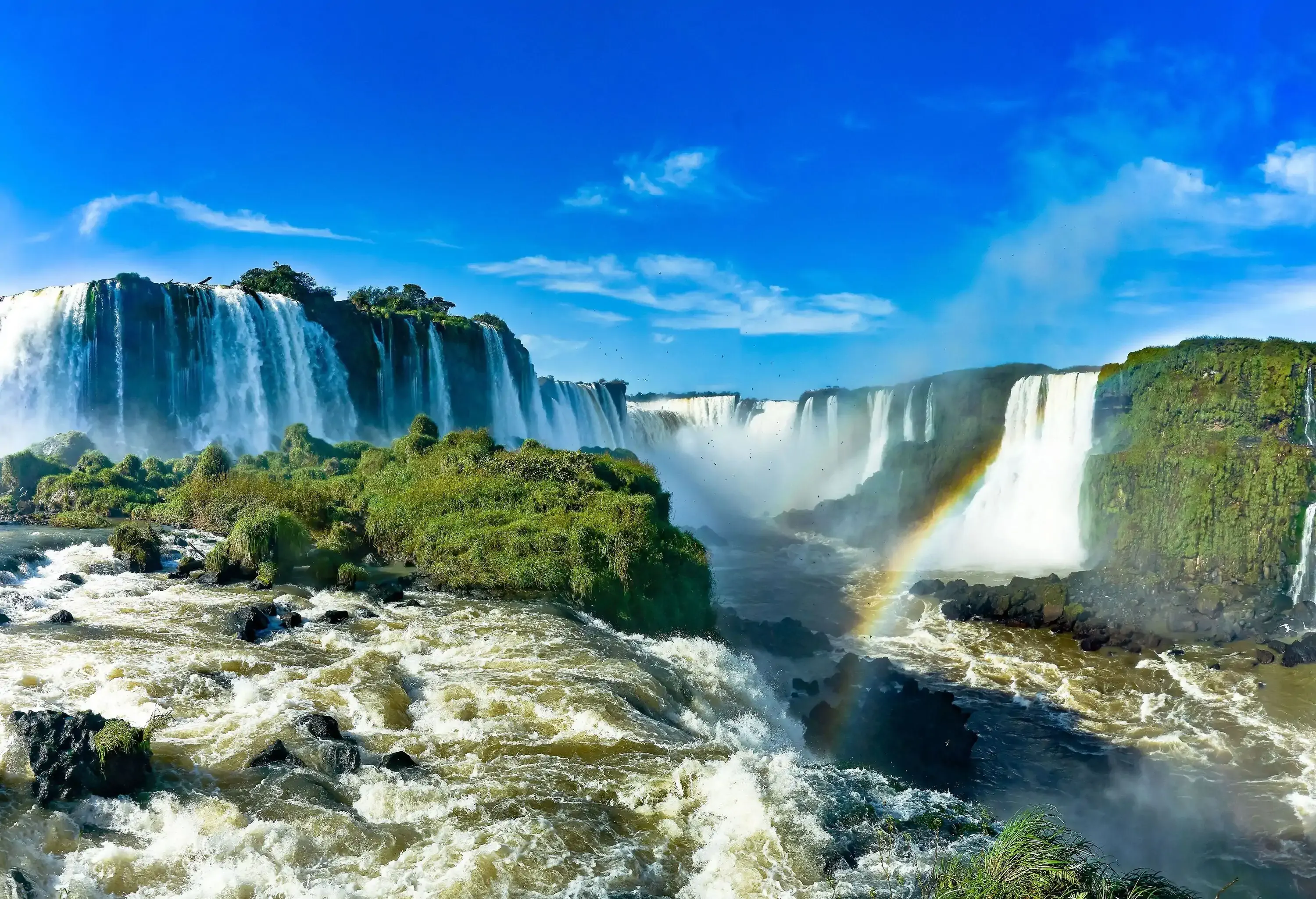 A rainbow flashing across a river surrounded by multiple waterfalls.
