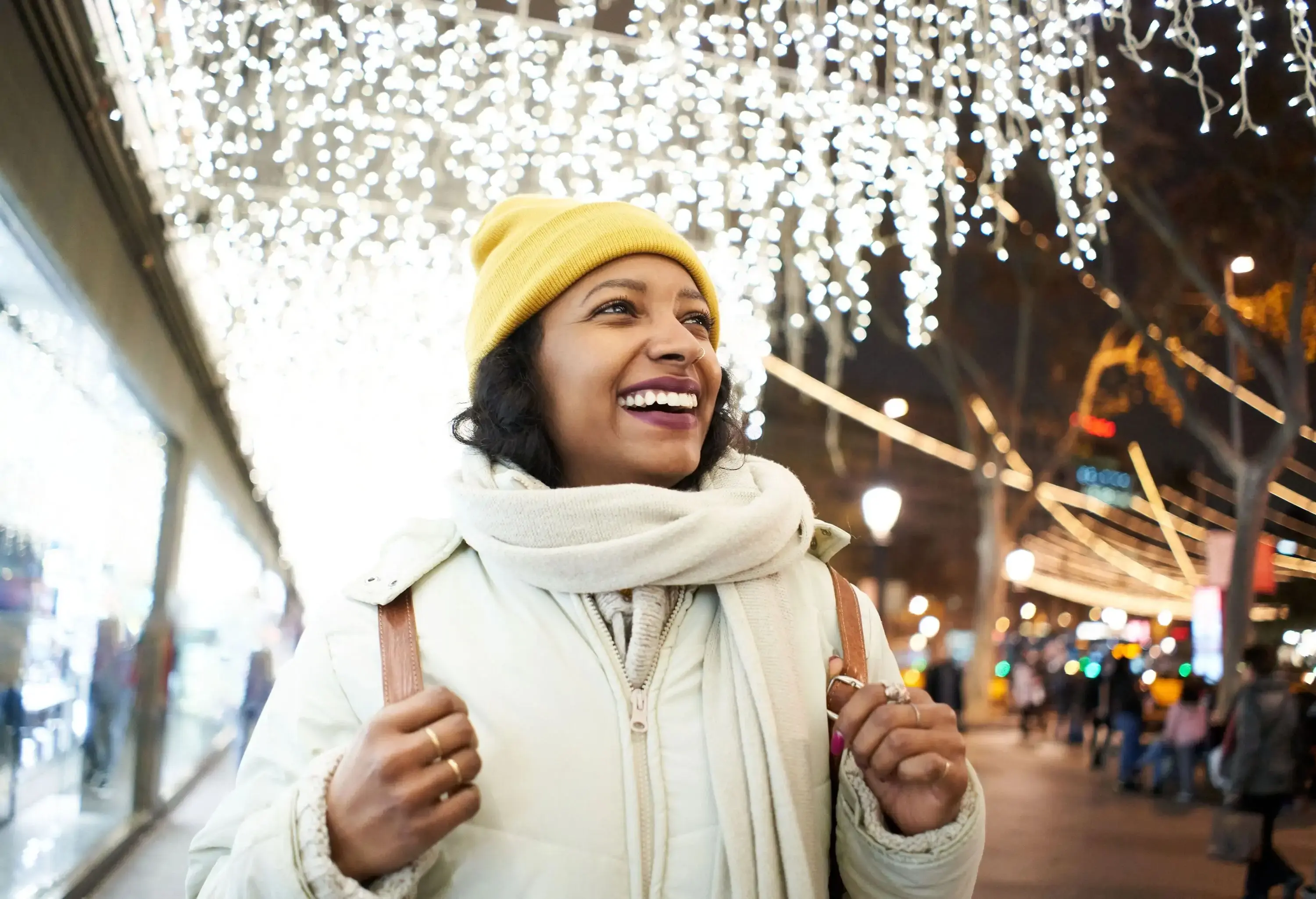 A happy female tourist wanders outdoors with lit Christmas lights.
