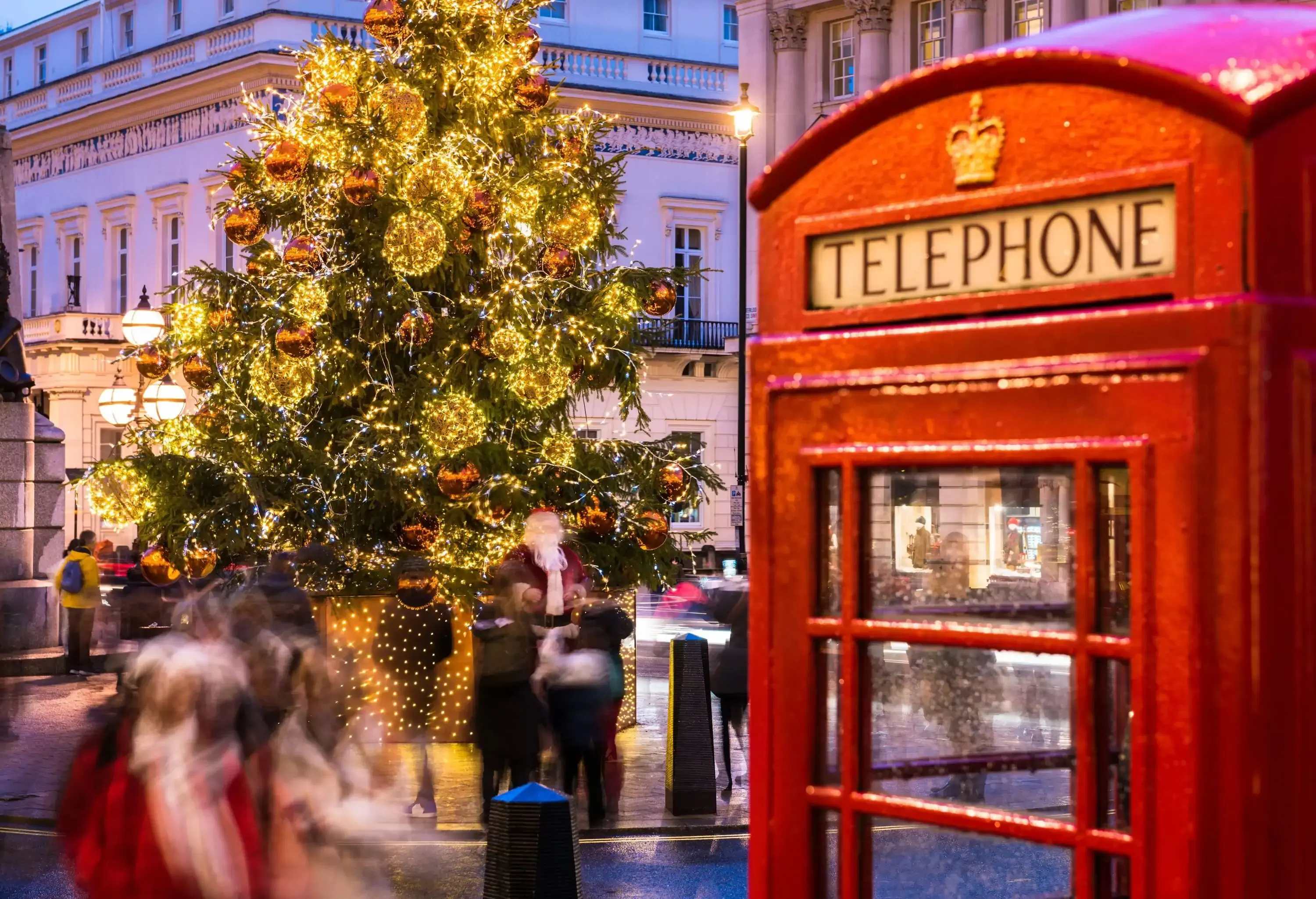 People in motion under giant illuminated Christmas lights and an iconic London telephone booth.