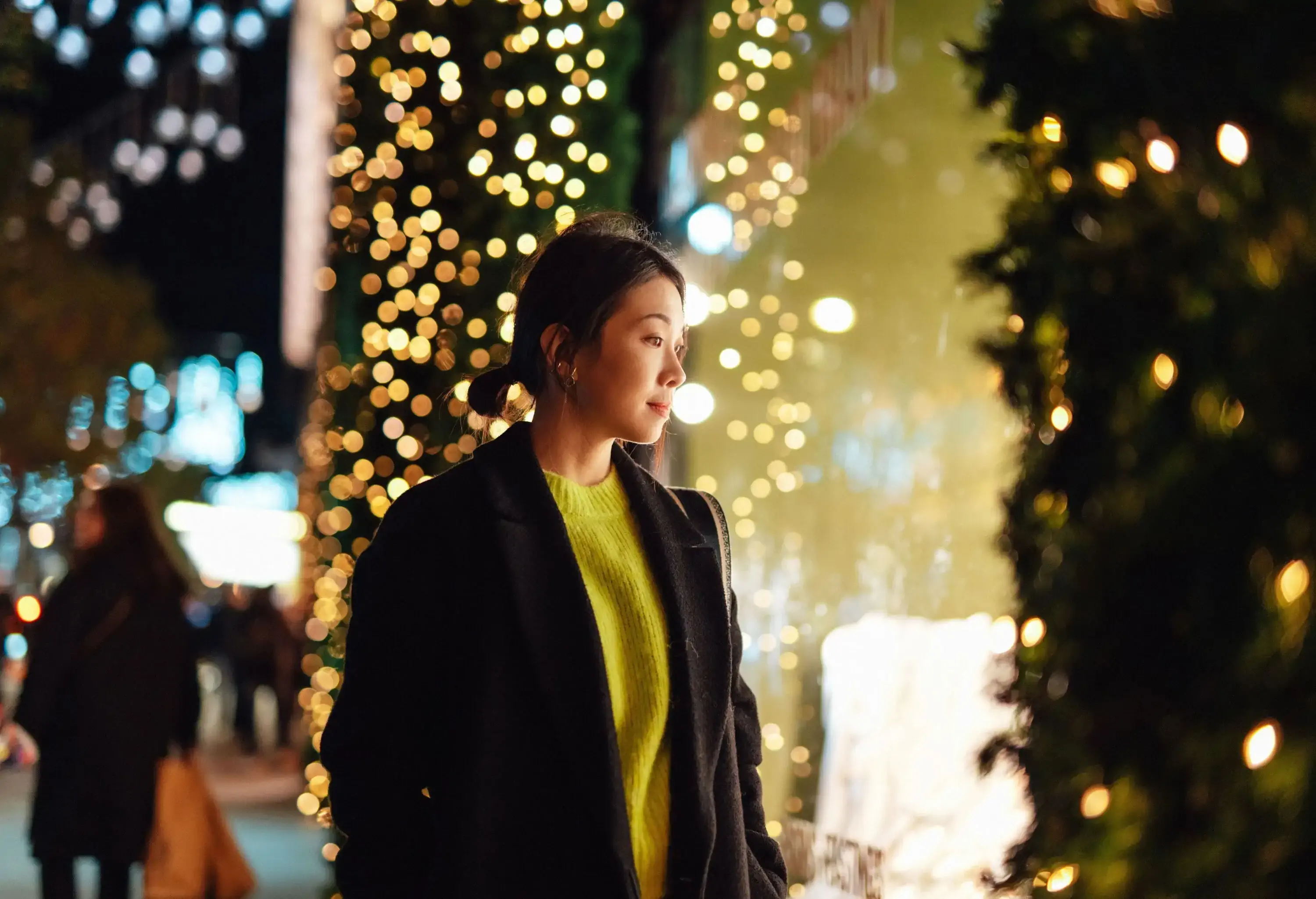 Asian woman look through shop window at night, with illuminated fairy lights in the background. Christmas shopping.