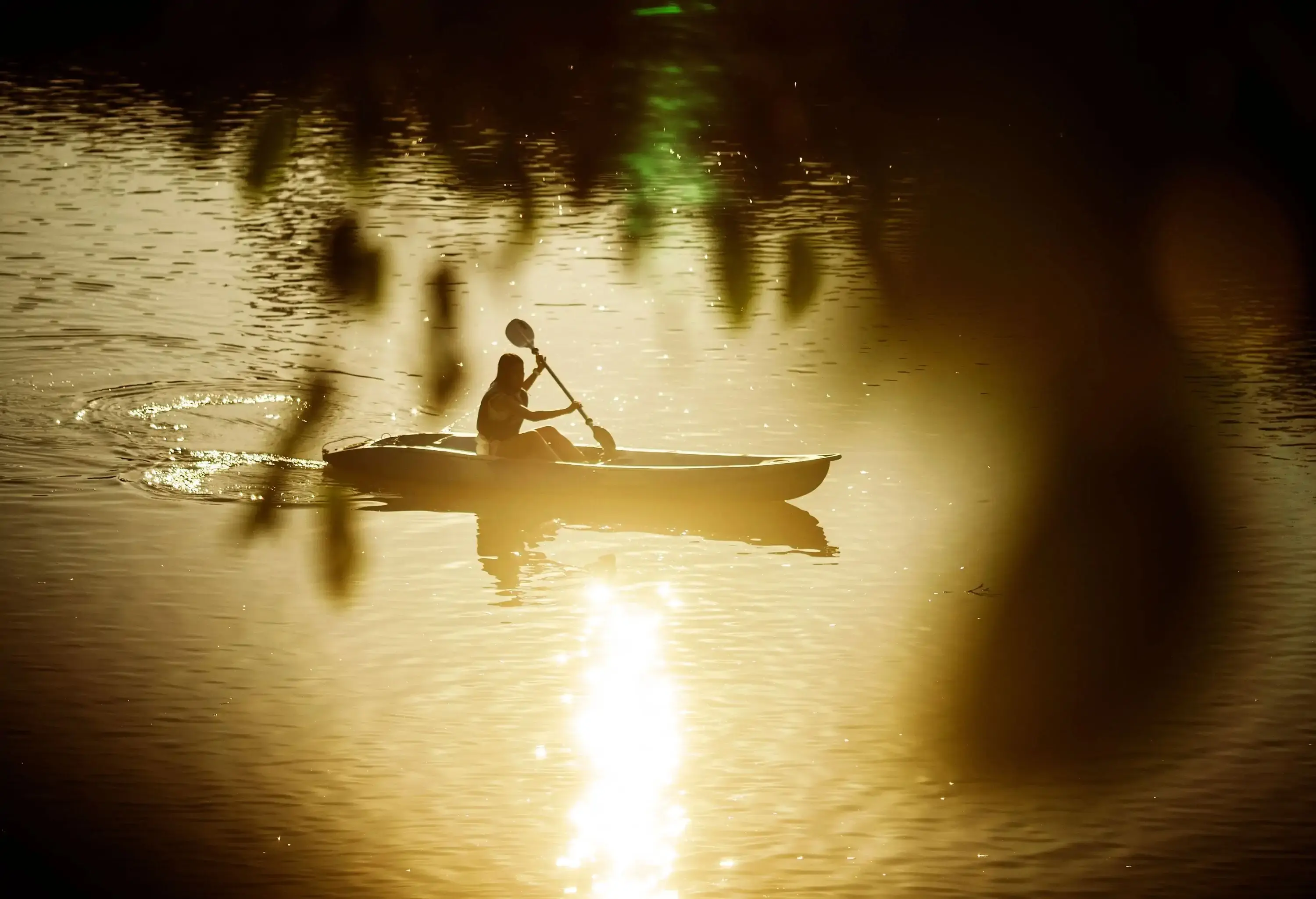 Silhouette of a person paddling on a canoe across a glistening lake.