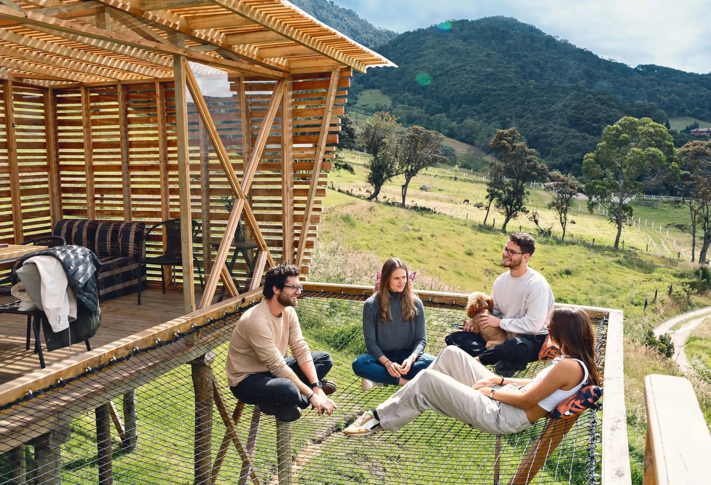 Four people hang out while sitting on the hammock floor of their glamping house suspended above the lush grassland.