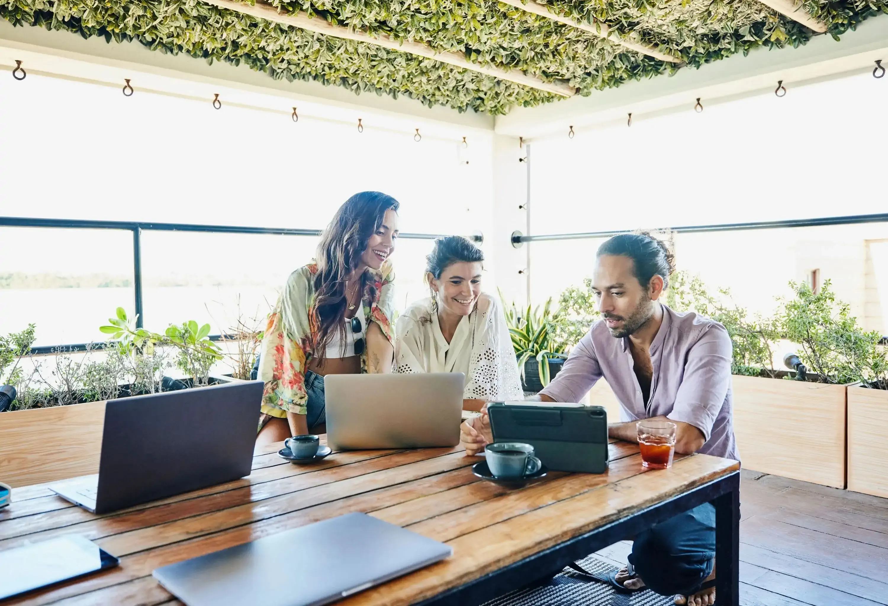 Medium wide shot of smiling colleagues discussing project on digital tablet while working remotely from deck of vacation rental