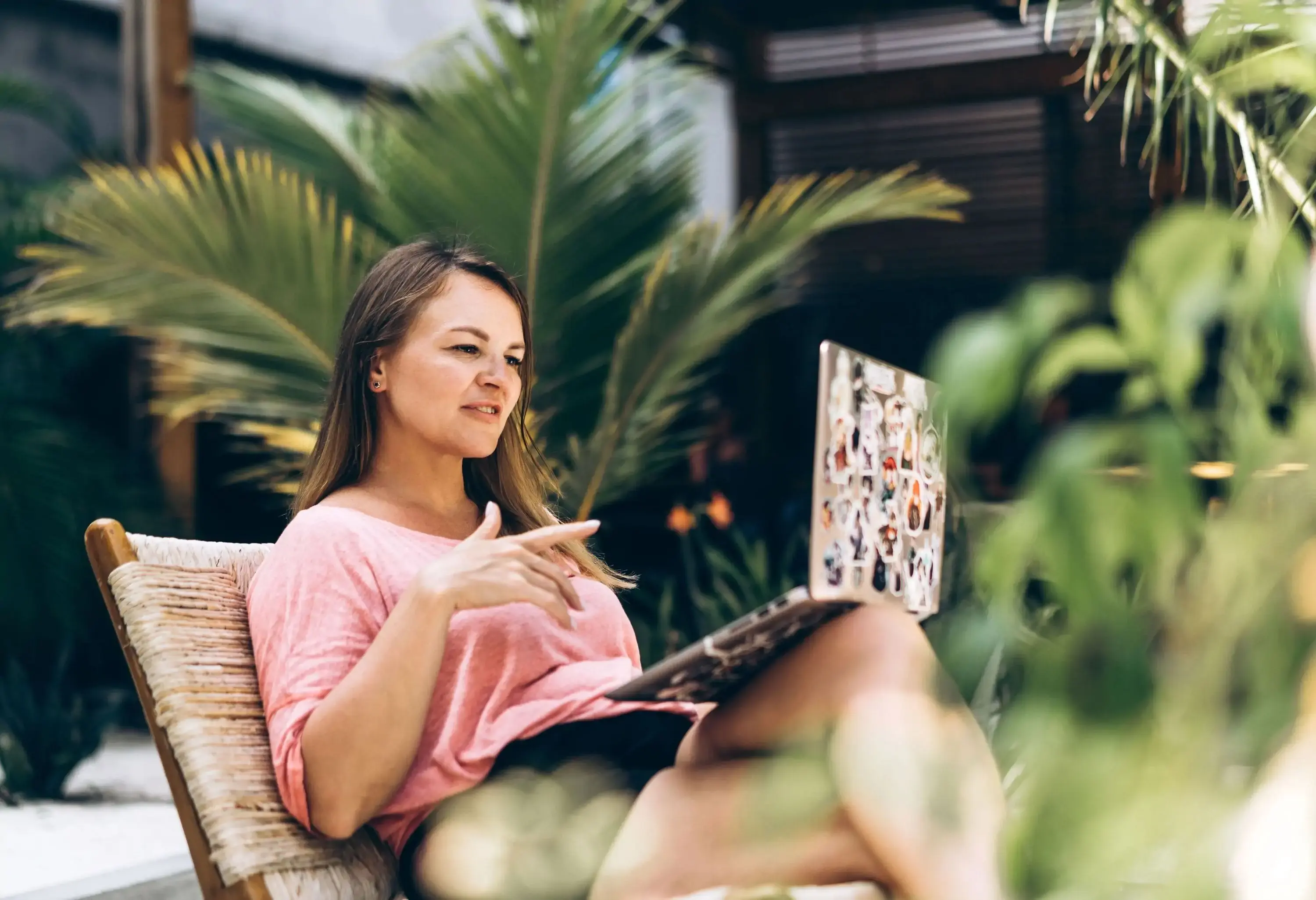 Woman sitting in front of a laptop in the beach cafe. Business trip or vacation in a high class tropical resort. Online shopping, booking, freelance working, consultation with a psychologist