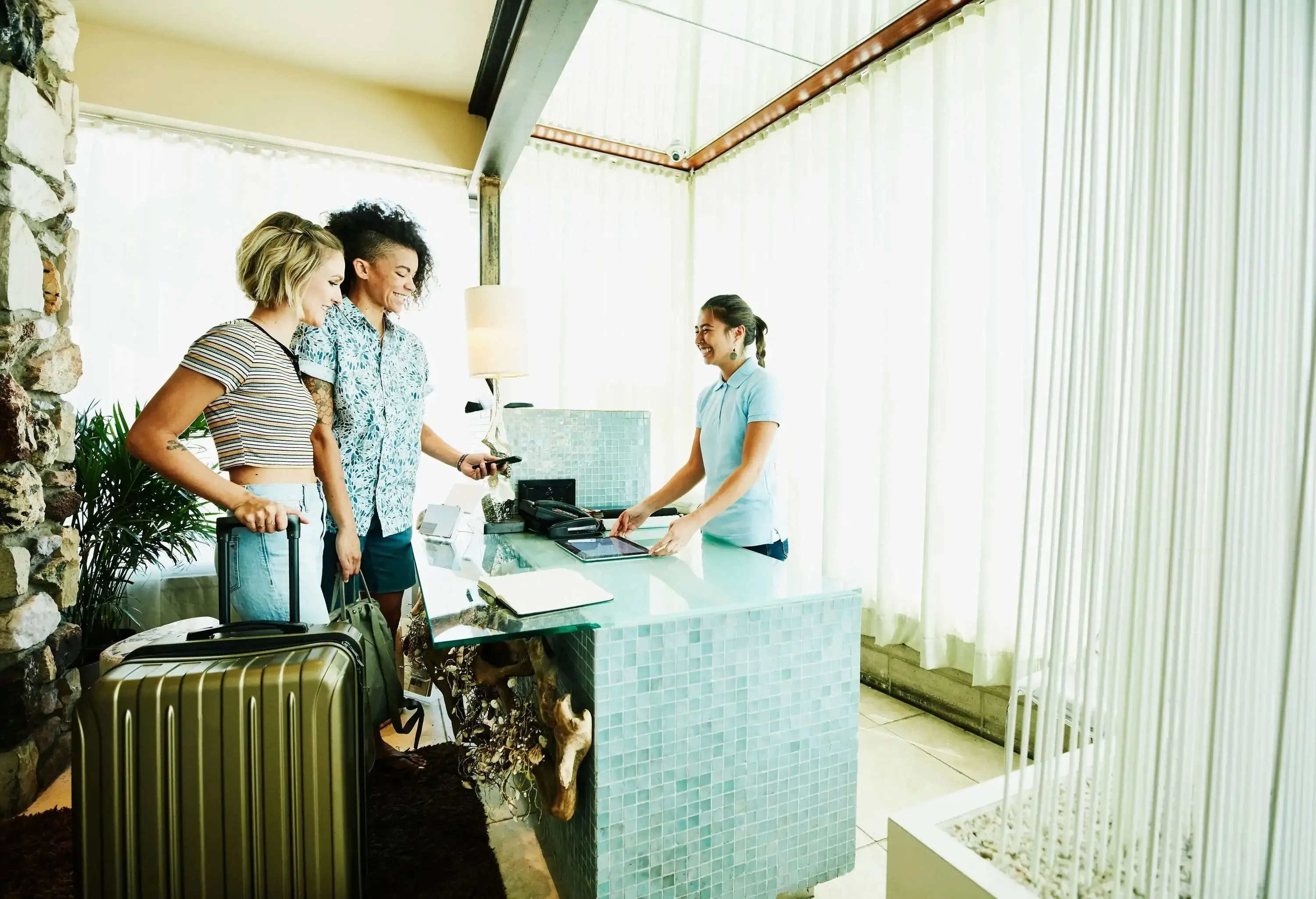 A happy couple with their luggage checks in at the counter of a hotel receptionist.