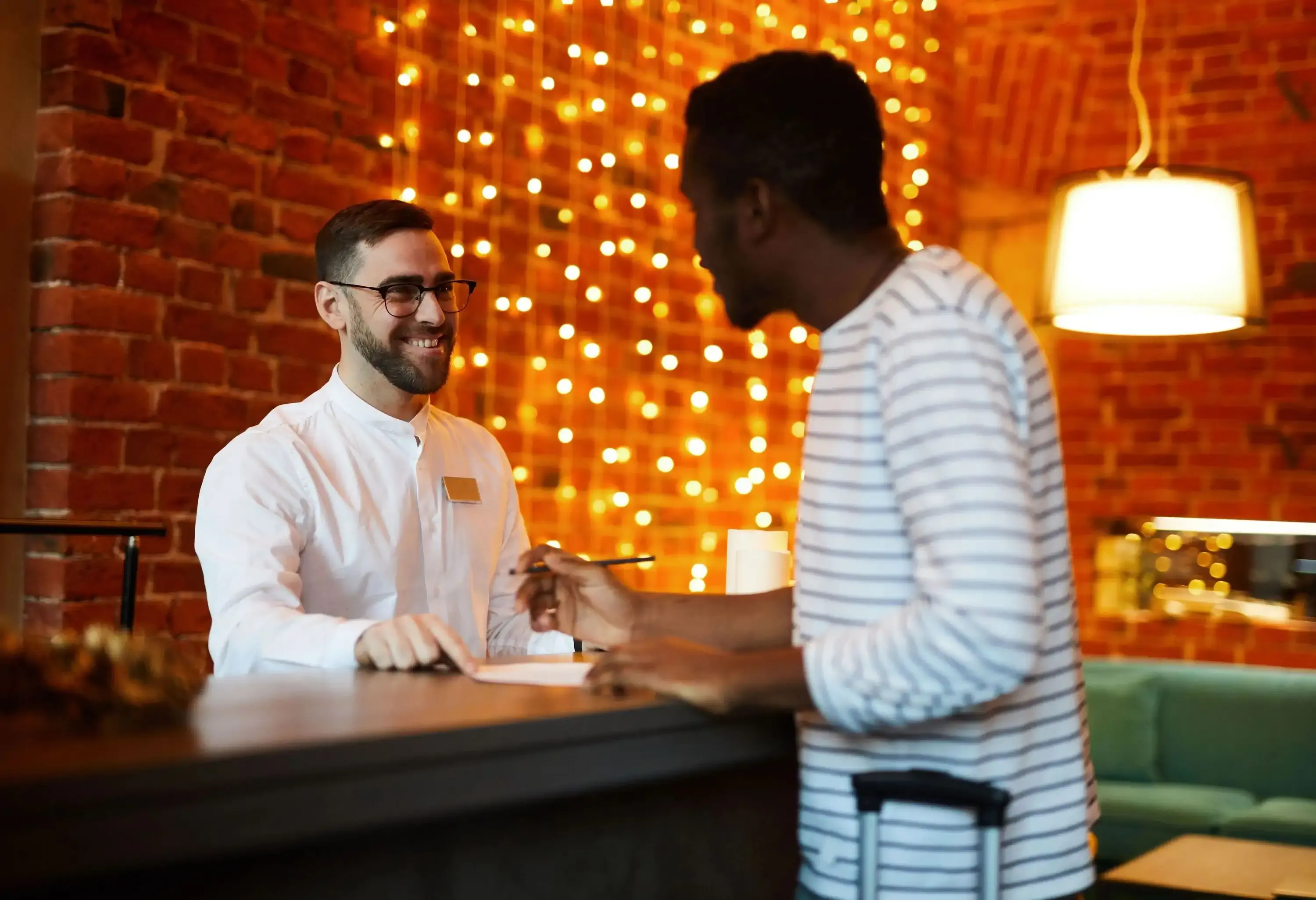 Happy hotel receptionist talking to guest by the counter and helping him to register