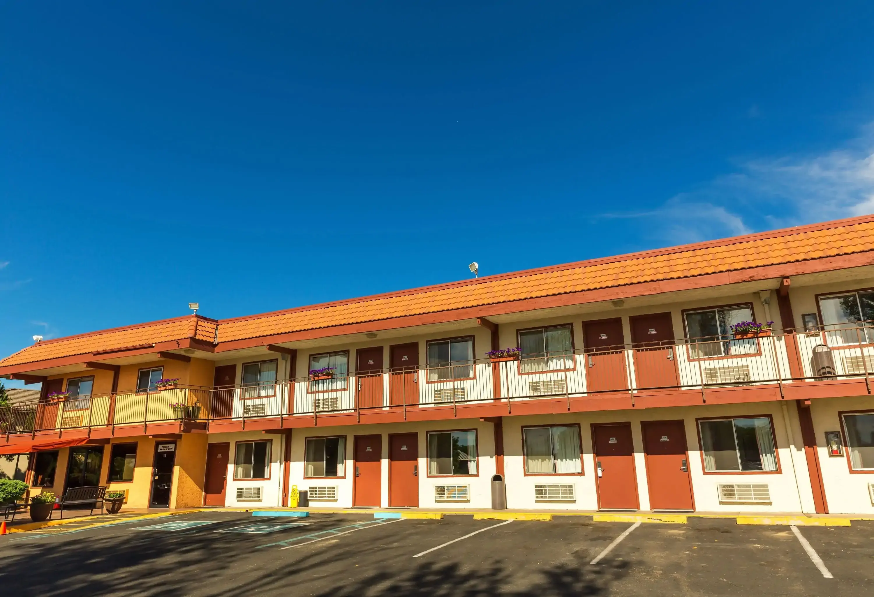 A two-level motel with white walls and brown doors in front of an empty parking lot.