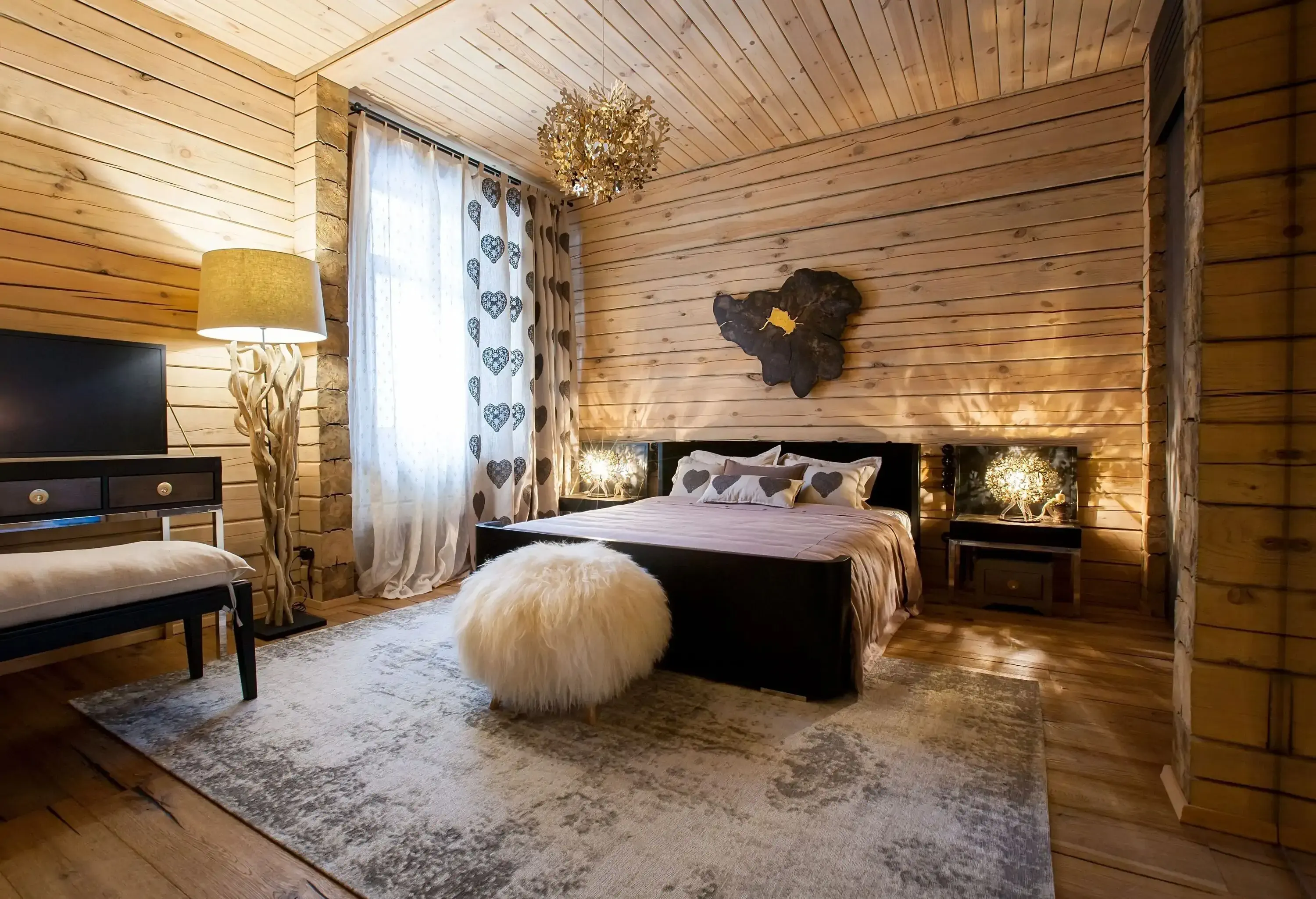 A bedroom with wooden panelling, a double bed on a rustic rug, a fur pouf, and a vanity set.