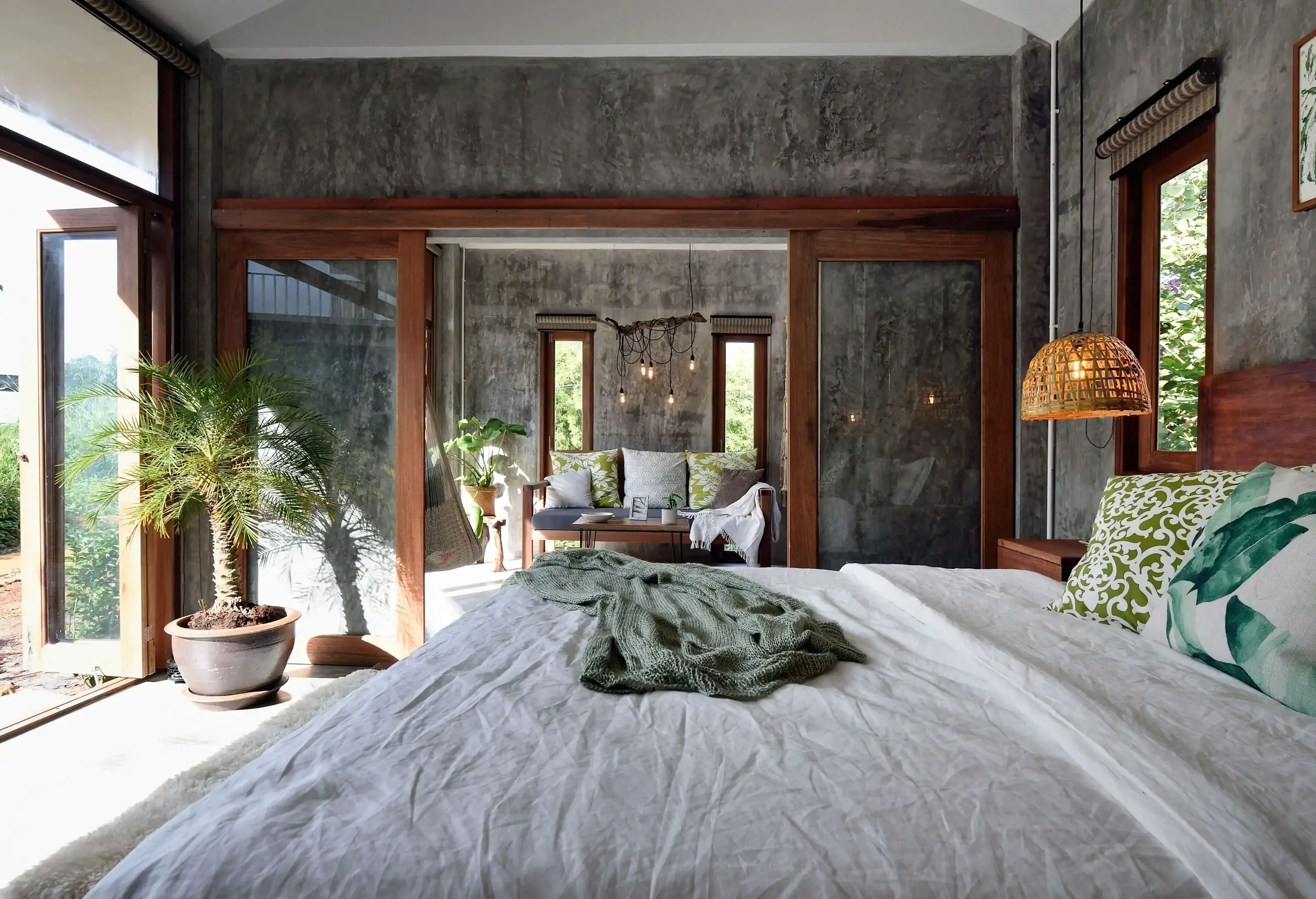 A grey-walled room with a cosy living room and a wide bed ornamented with a potted plant.