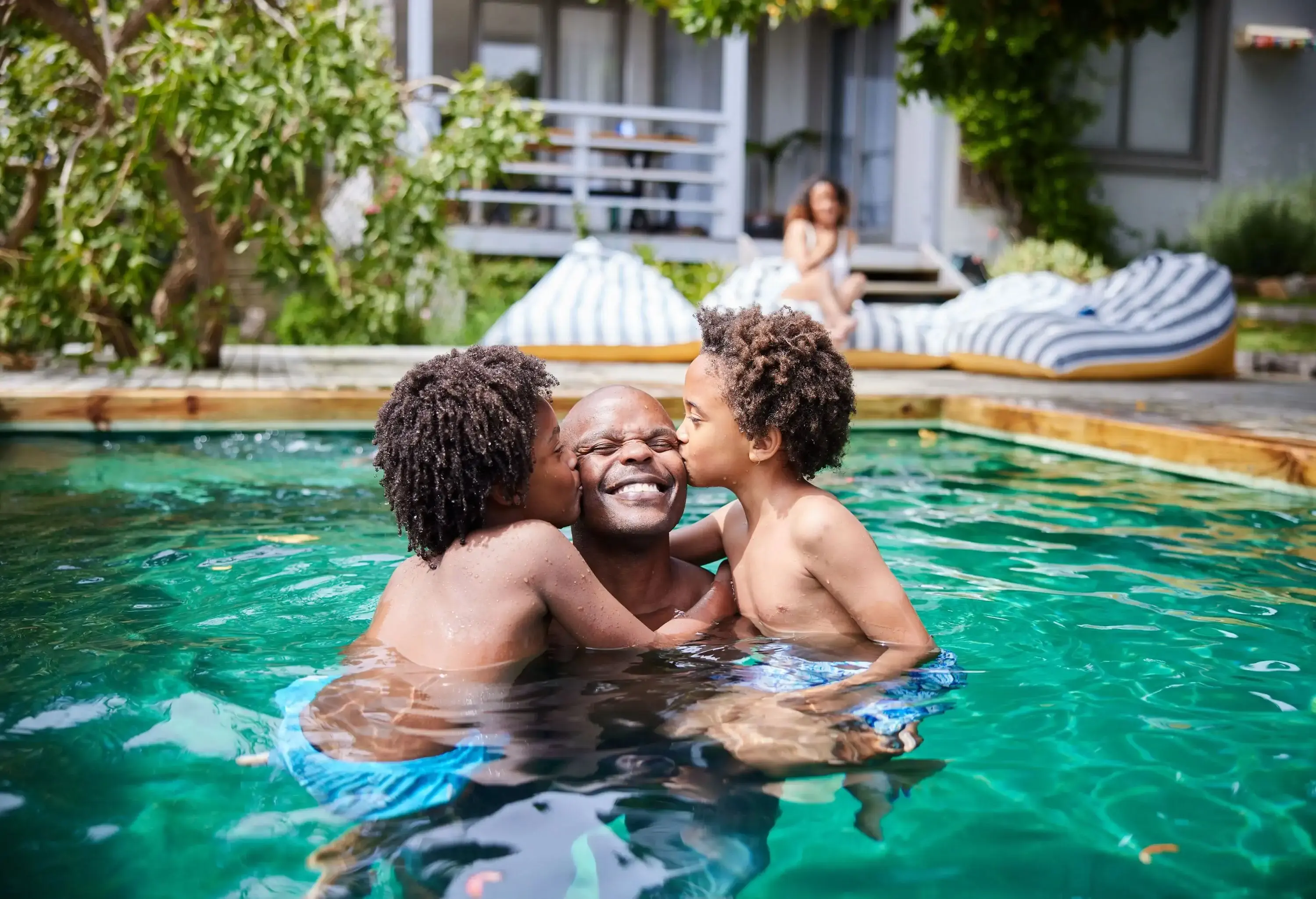 Young children kissing their dad while playing together in a swimming pool