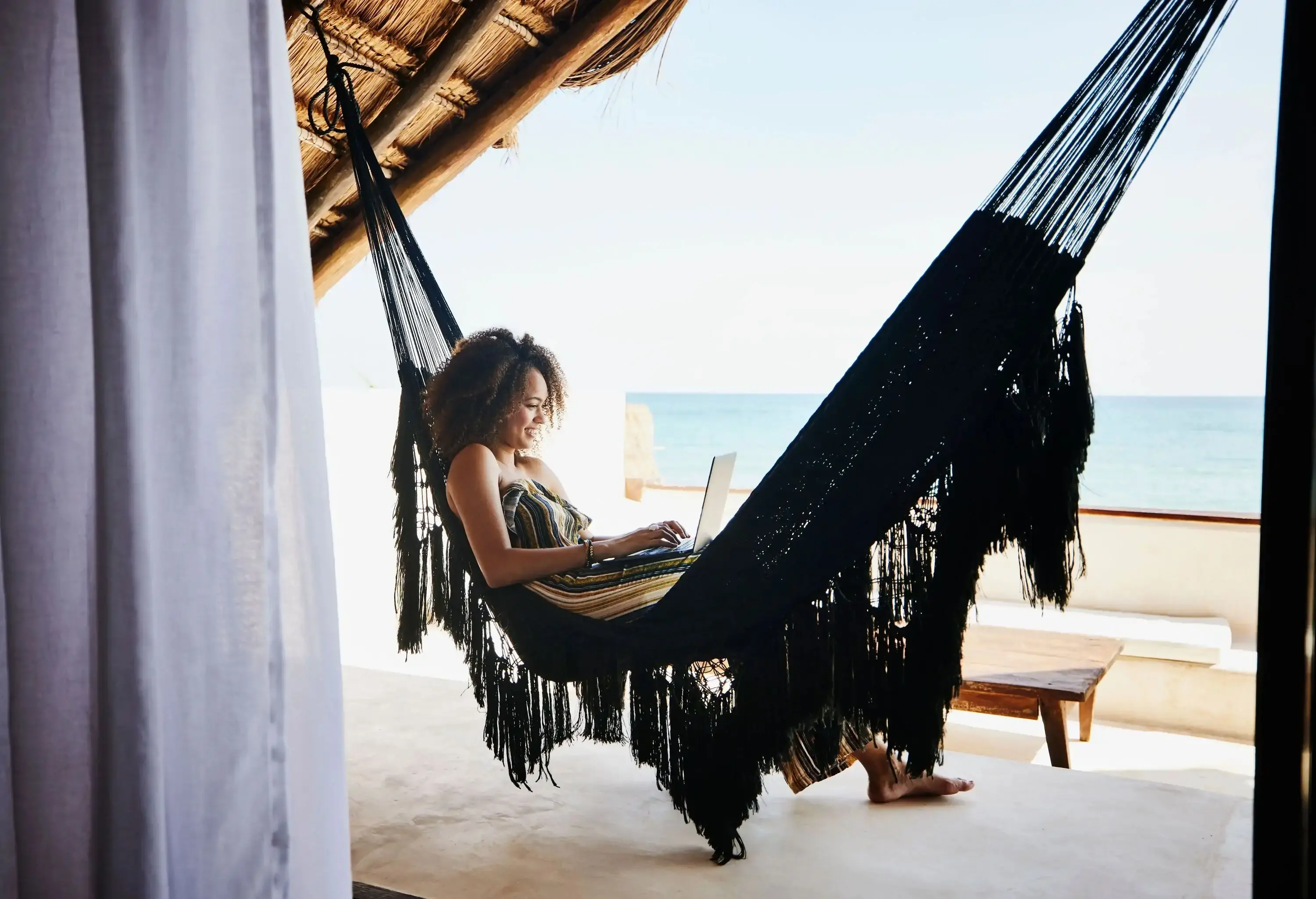 Woman working on laptop on a hammock in a hotel by the beach