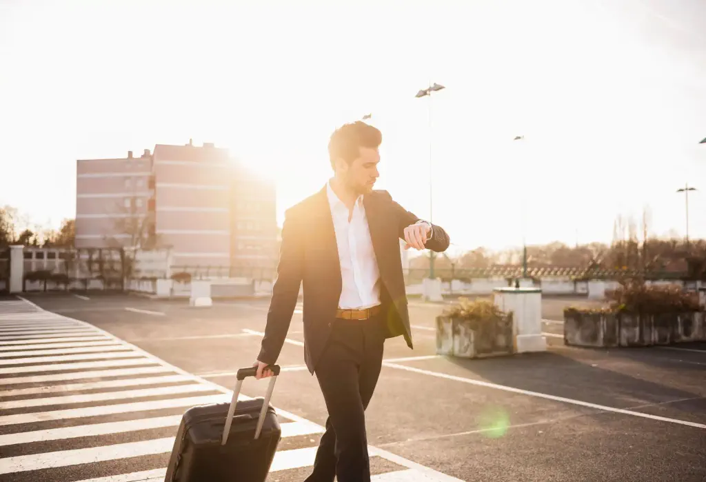 A sharply dressed individual, carrying their luggage, strides purposefully across an empty parking lot.