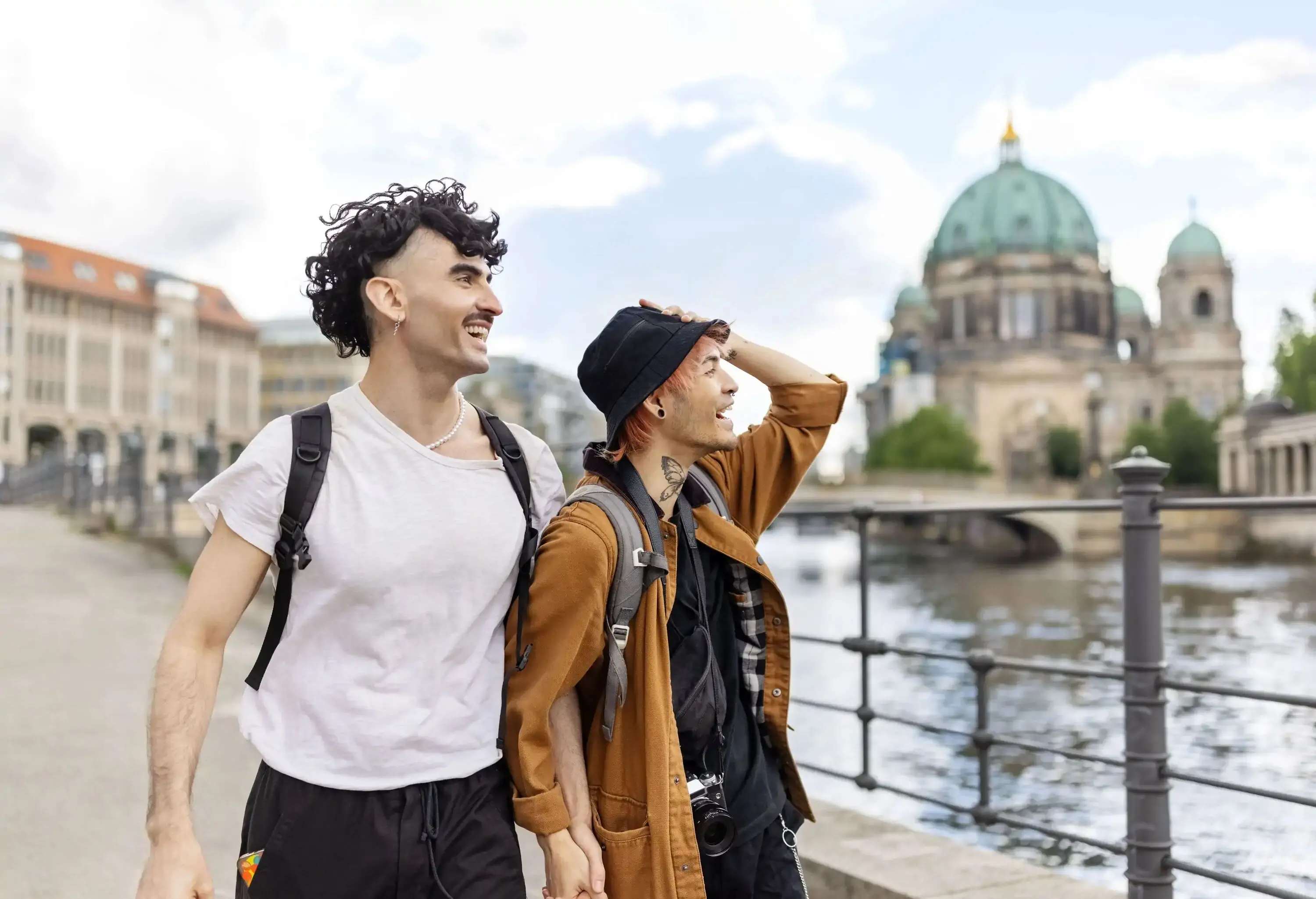 Couple strolling together along the riverbank with a large domed building in the background.