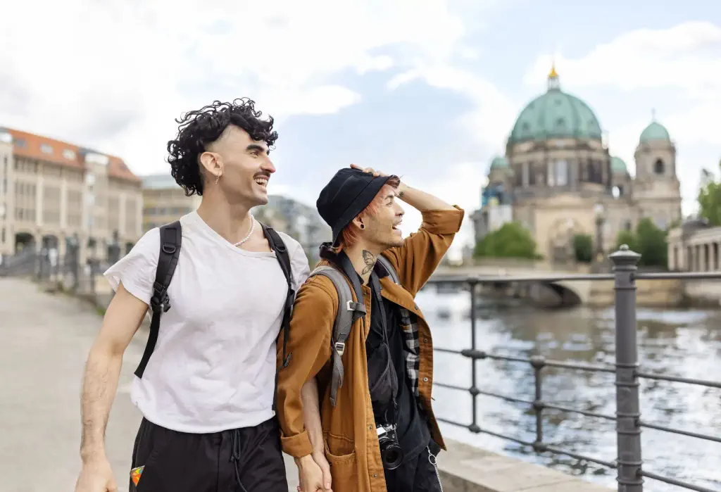 Couple strolling together along the riverbank with a large domed building in the background.