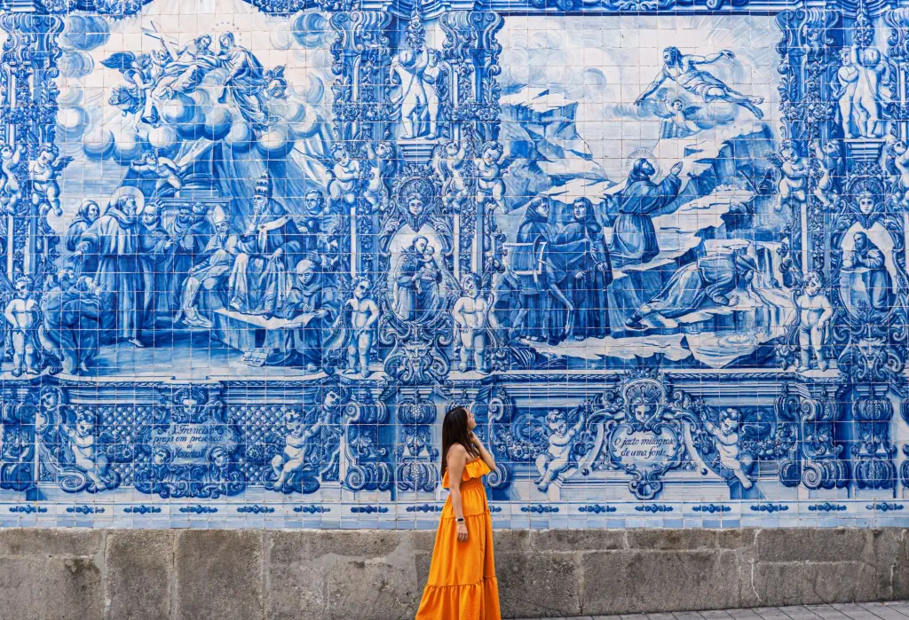 Woman wearing an orange dress standing on a streetwalk  wondering at wall tiled with traditional azulejos