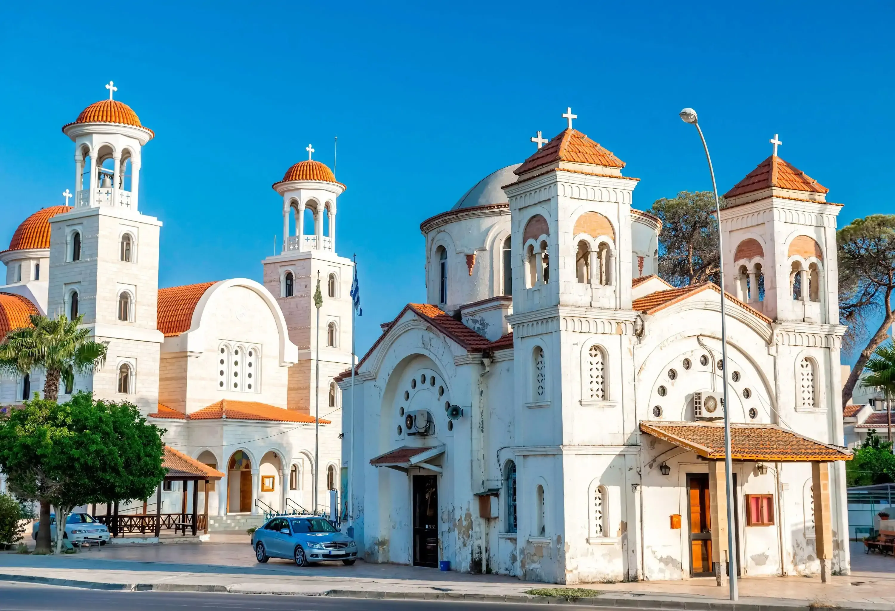Two white churches with twin bell towers each, one with red tile hip roofs and the other with red tile dome roofs.