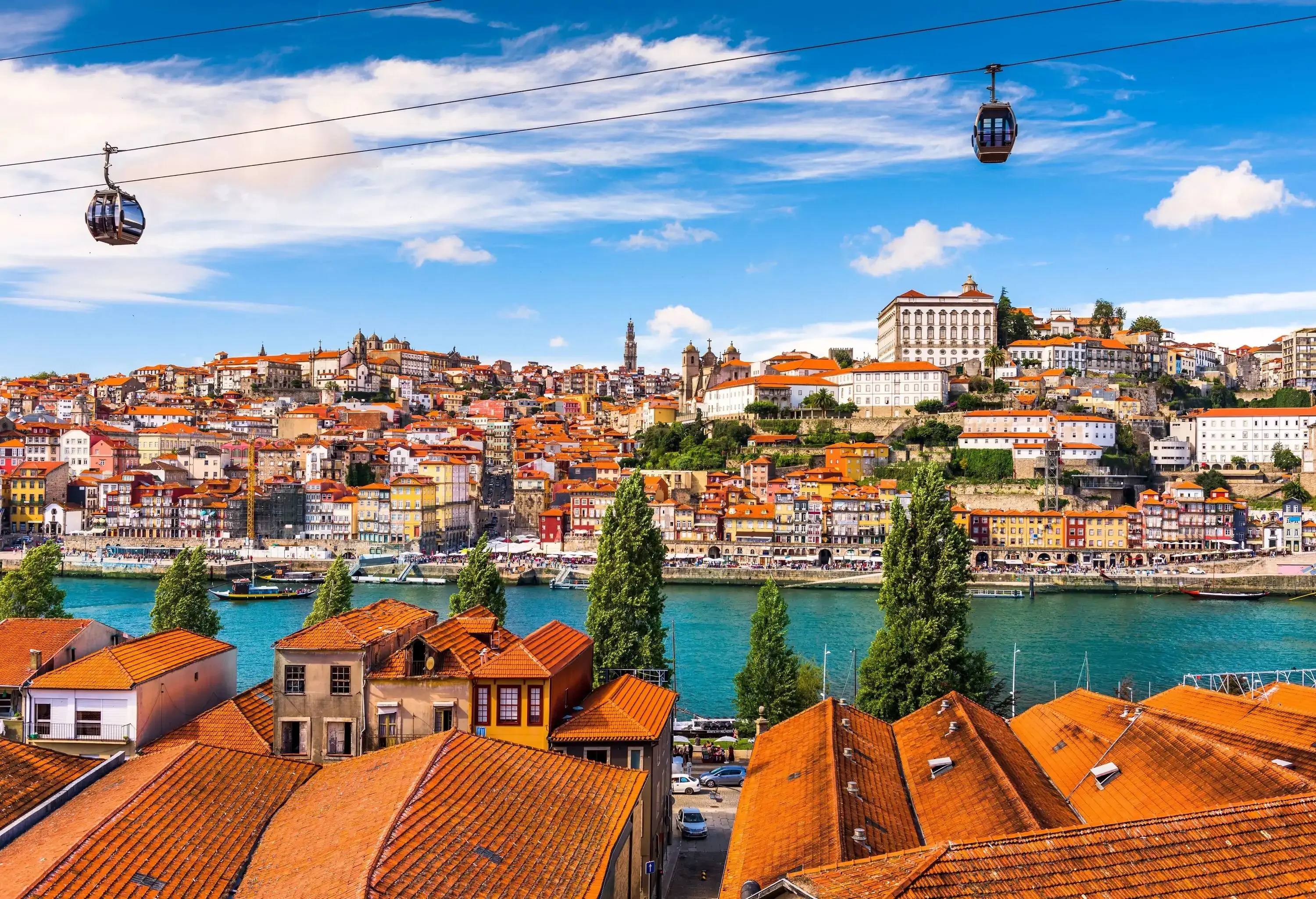 Two cable cars travel above a residential area along a river with cityscape views.