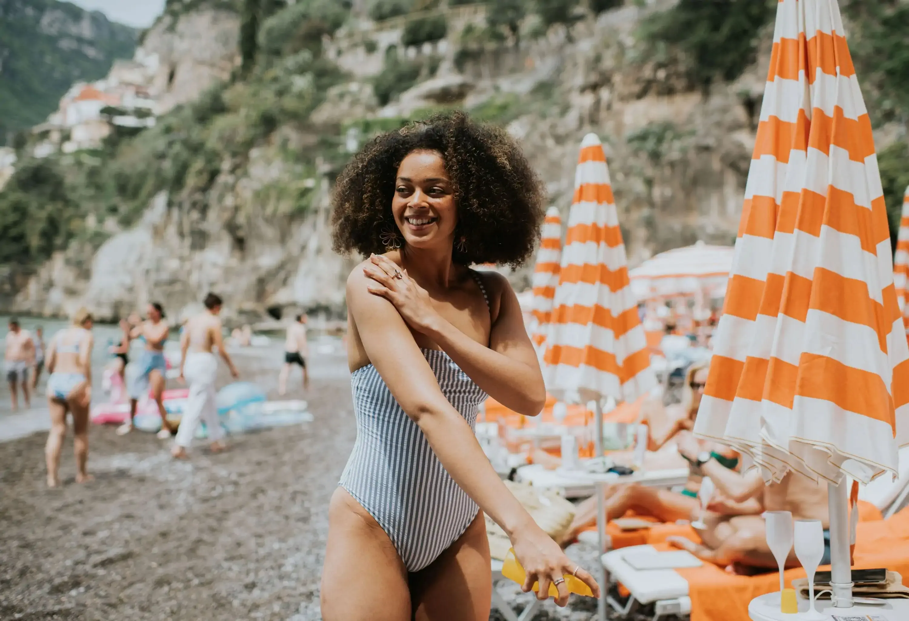 Smiling young woman standing amidst orange and white striped beach umbrellas.