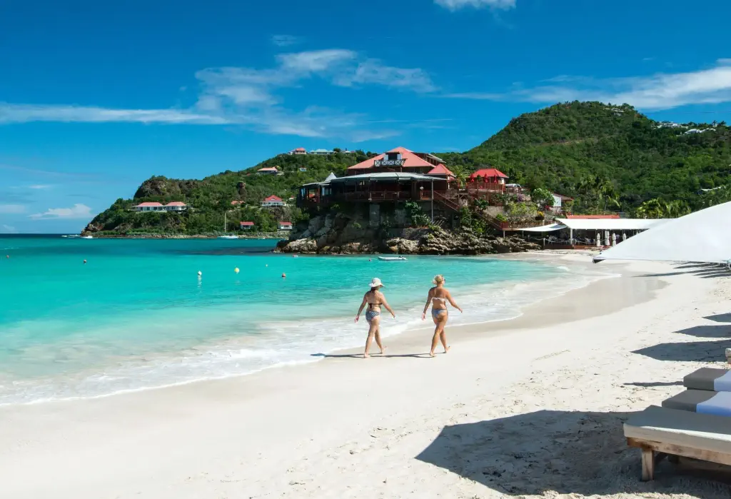 Two women in bikinis strolling down a white sand beach.