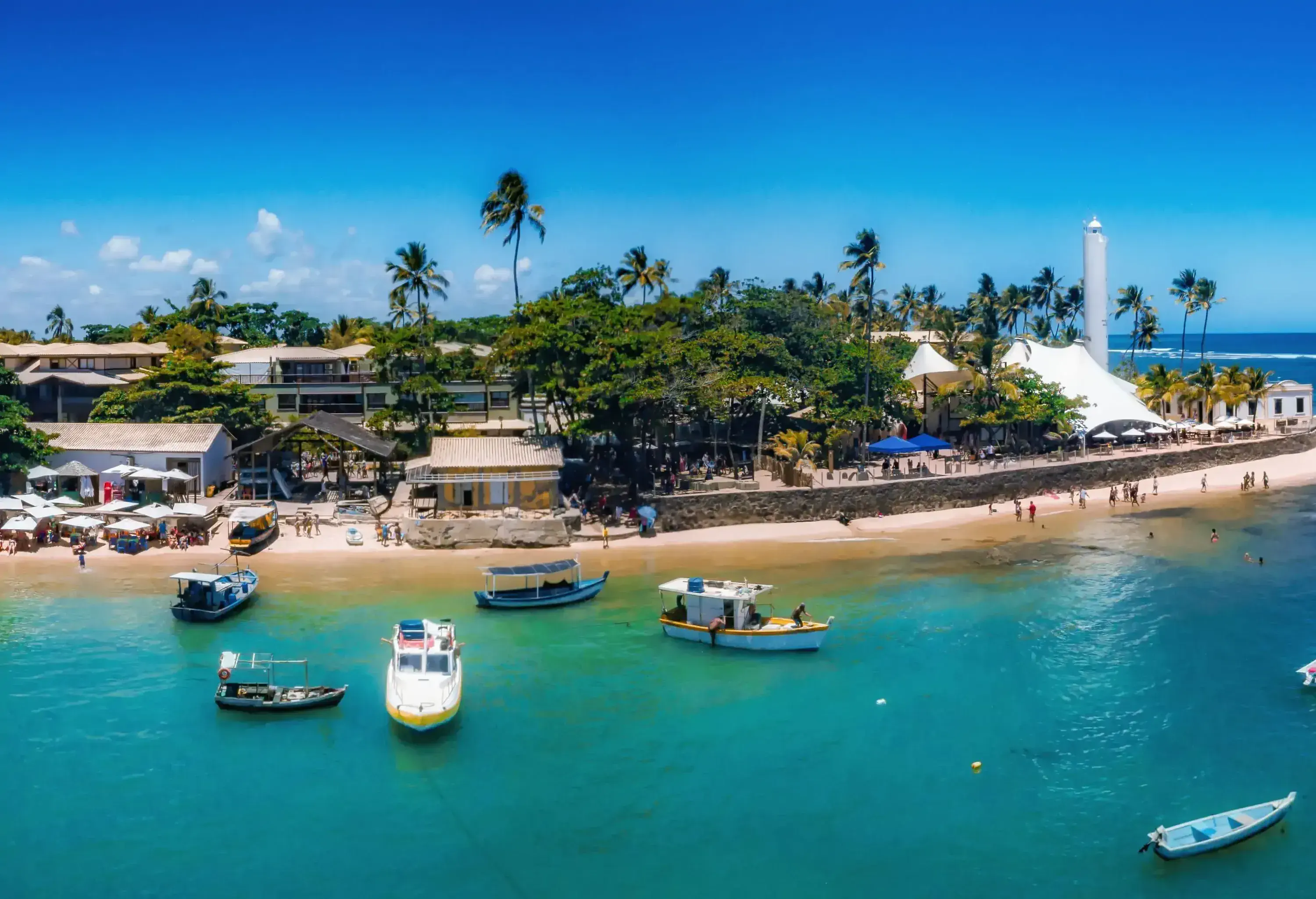 Aerial panoramic view of a coastal town and moored boats in the turquoise sea against the clear blue sky.