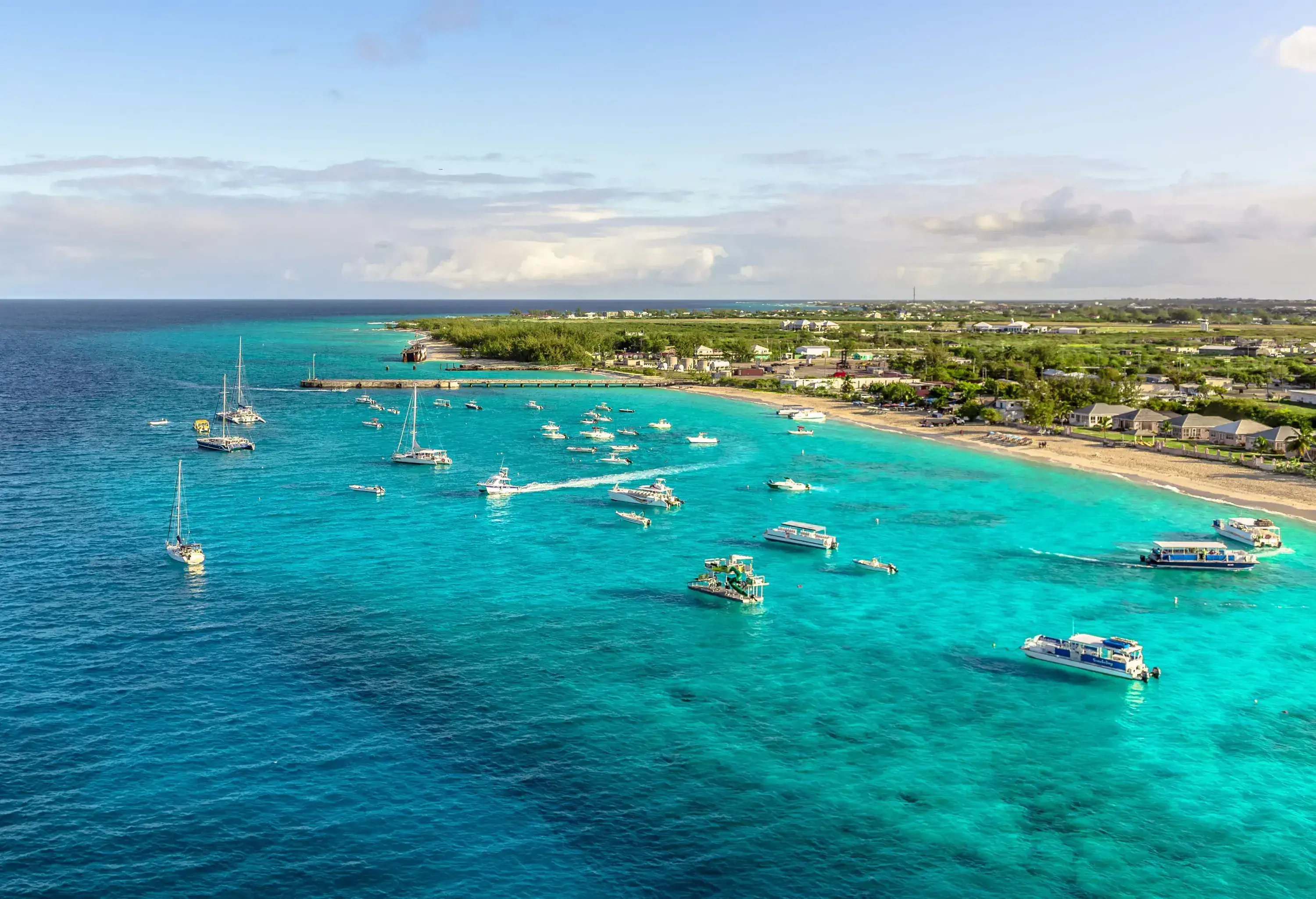 Aerial view of a tropical beach with turquoise water dotted with white boats by the lush island.