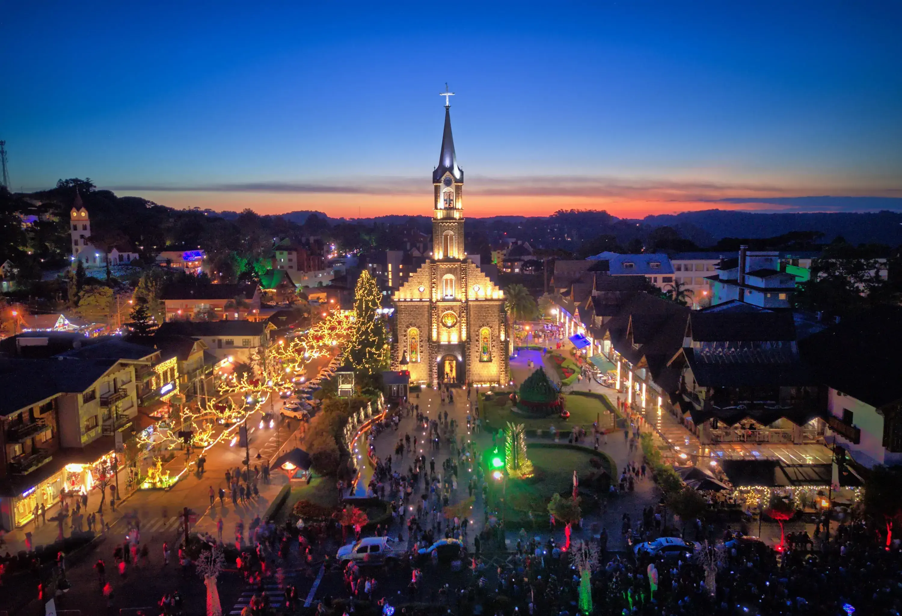 Aerial view of Saint Peter's Church in Gramado, Brazil lined with colourful LED lights and a bustling crowd.