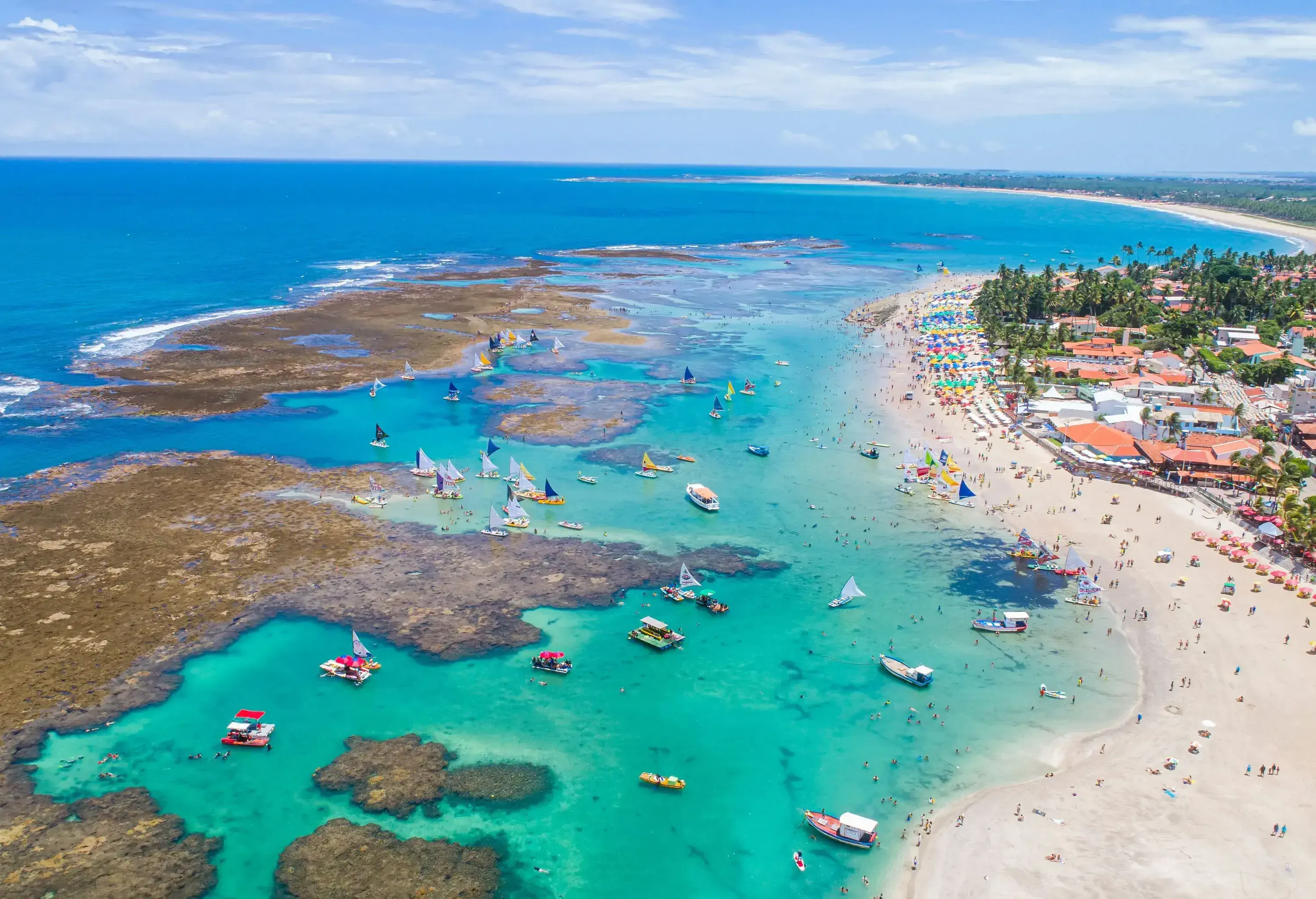 Boats floating around a wide coral reef structure that stretches over the turquoise sea.