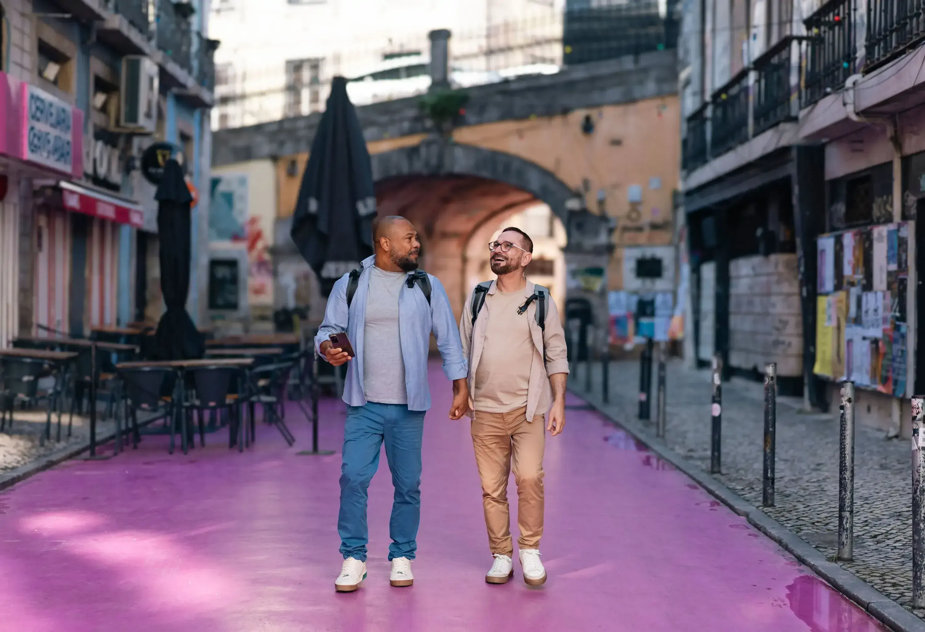 Two persons walking together on a sidewalk, framed by buildings and urban scenery.