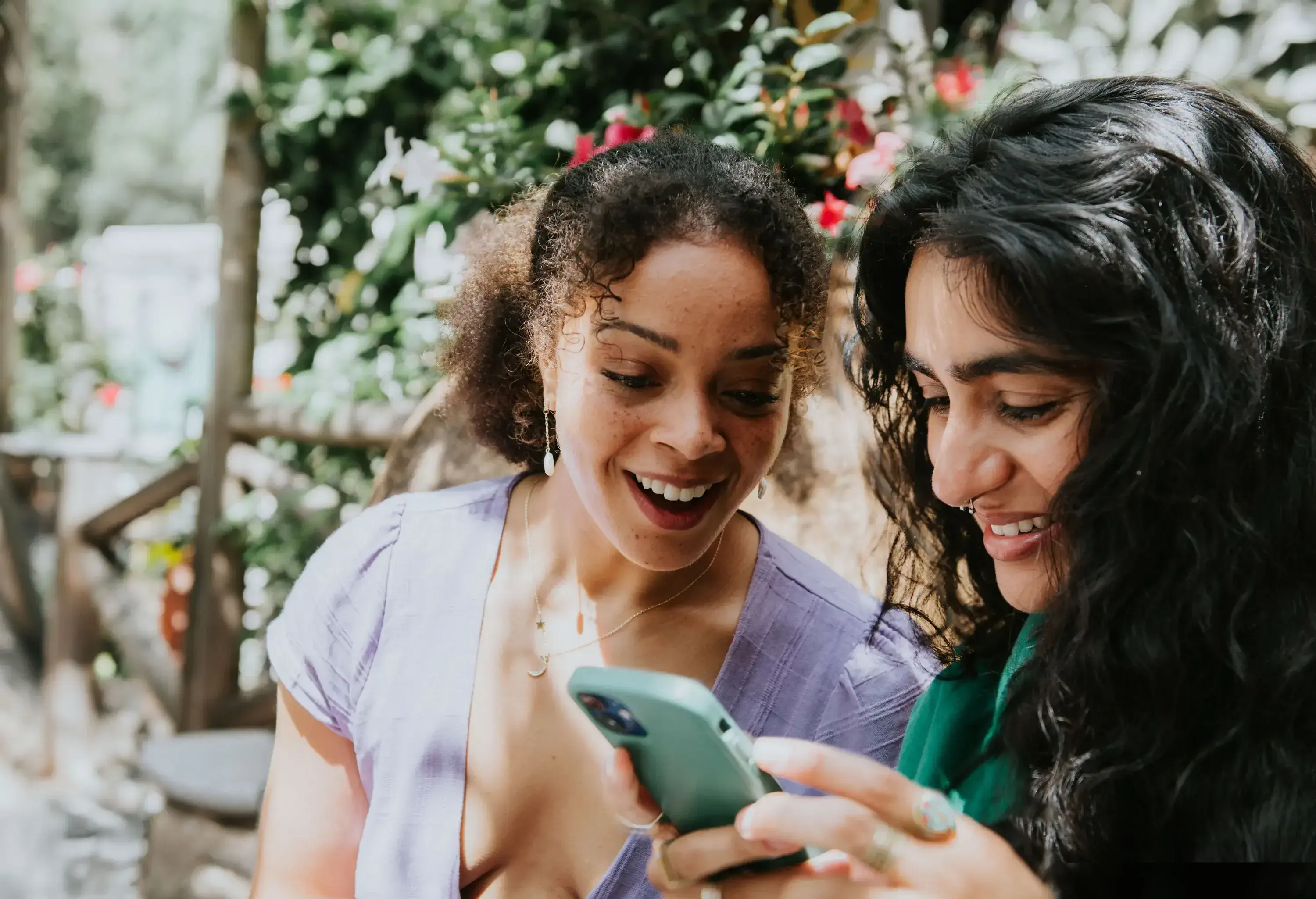 Two women laughing and smiling while intently focused on a smartphone.