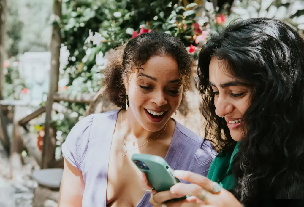 Two women laughing and smiling while intently focused on a smartphone.