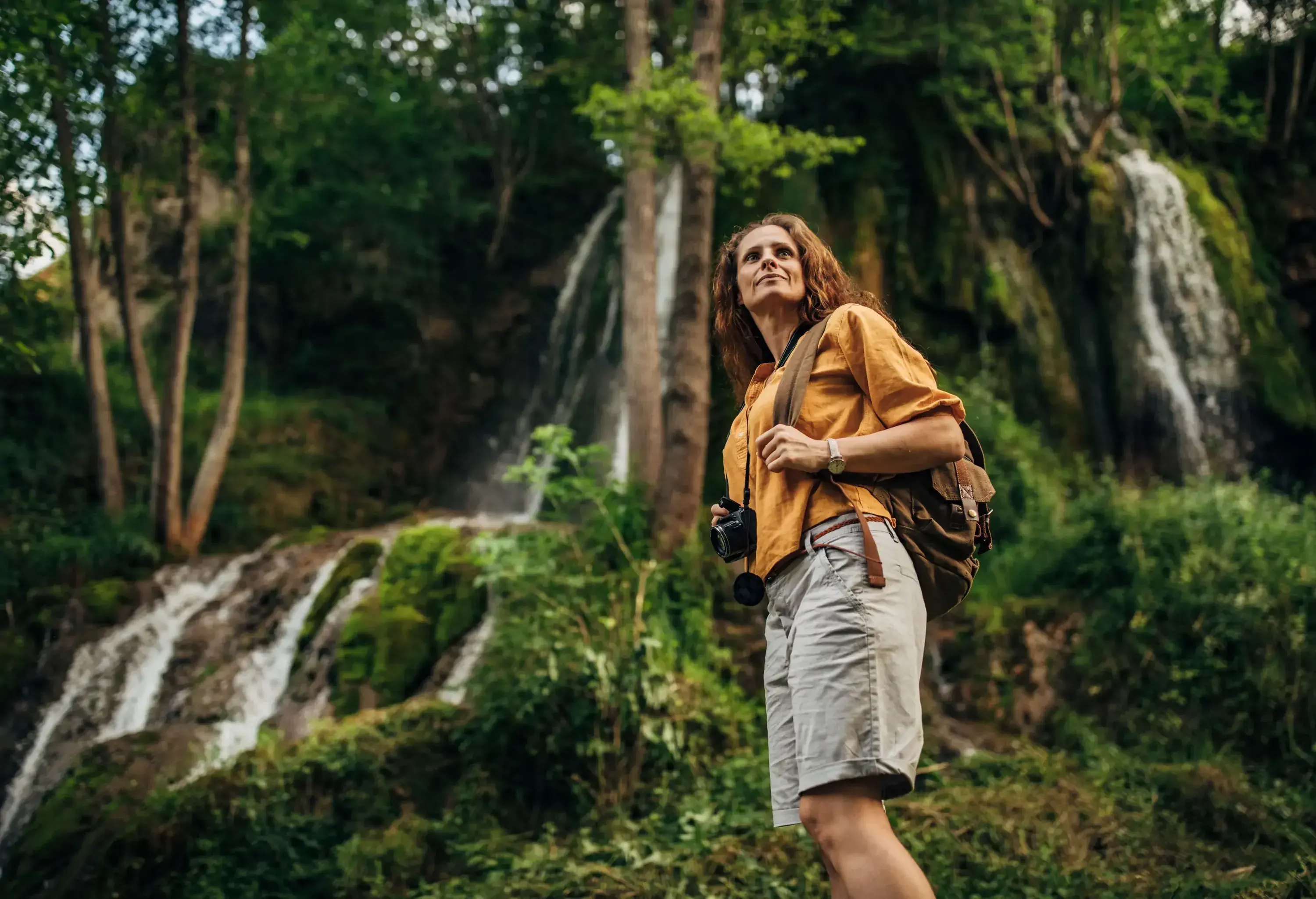 A woman hiking in the woods with a camera and a backpack.