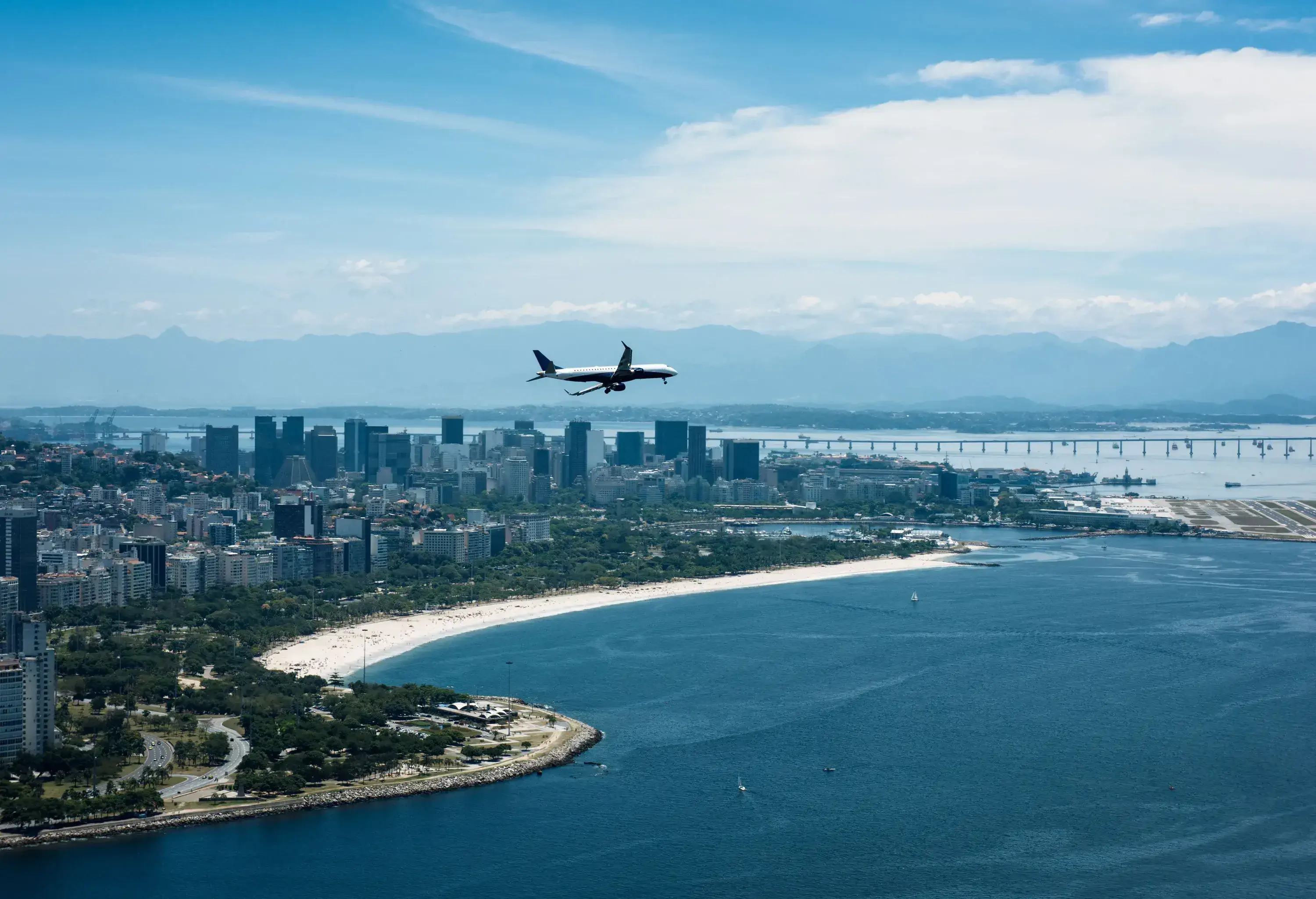 An airplane is flying over the deep blue sea against the city skyline.
