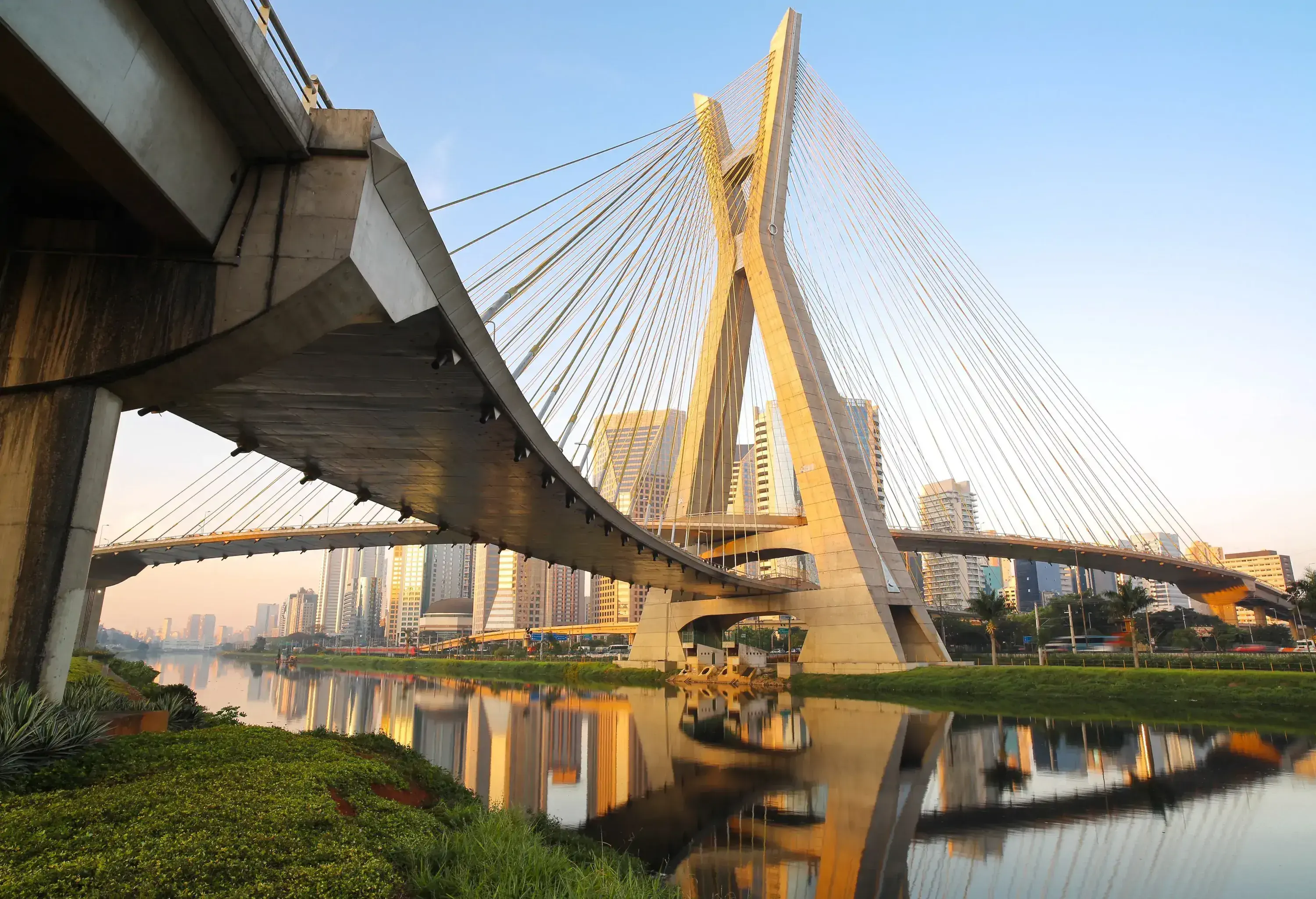 A suspension bridge across a calm river against the backdrop of the city skyline.