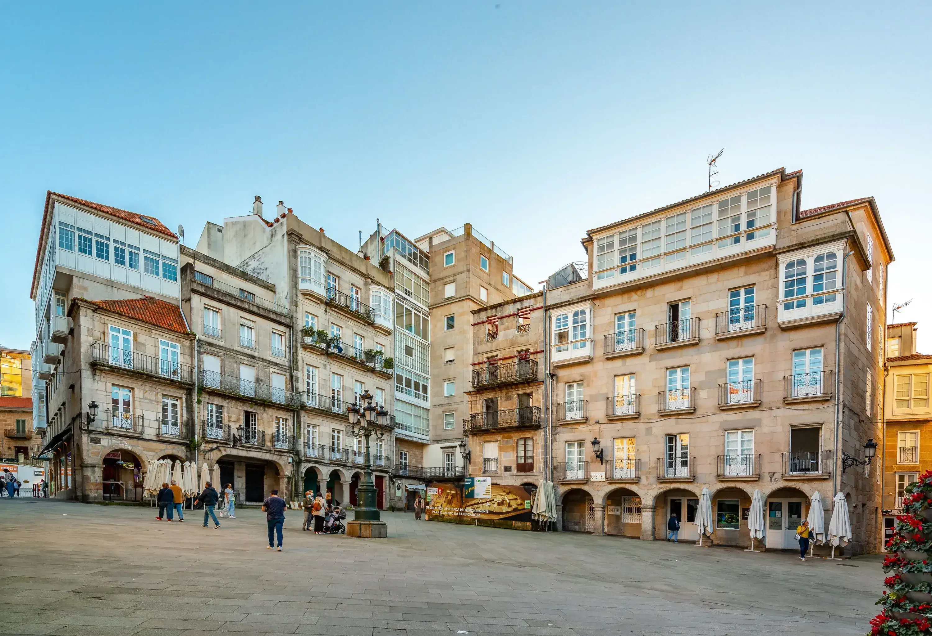 People stroll in a city square surrounded by classic buildings with small window balconies.