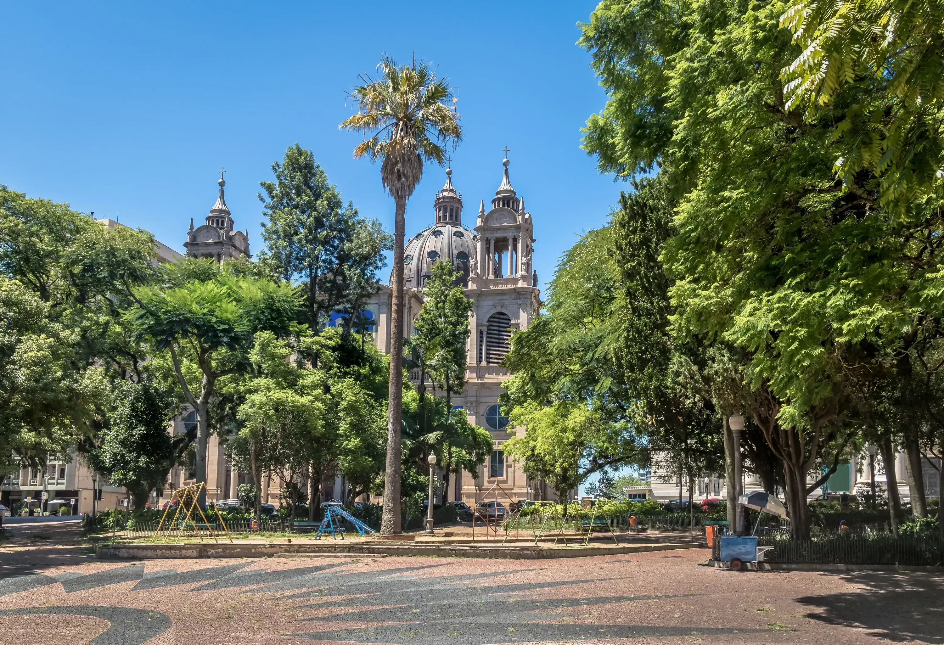 The church with two towering spires and a magnificent domed centre is partially obscured by a canopy of lush trees.