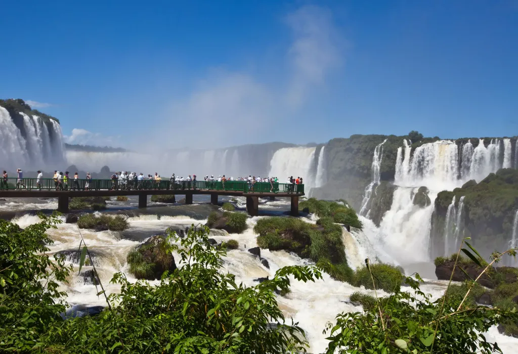 A crowd strolling through a boardwalk encircled by a gigantic waterfall system.