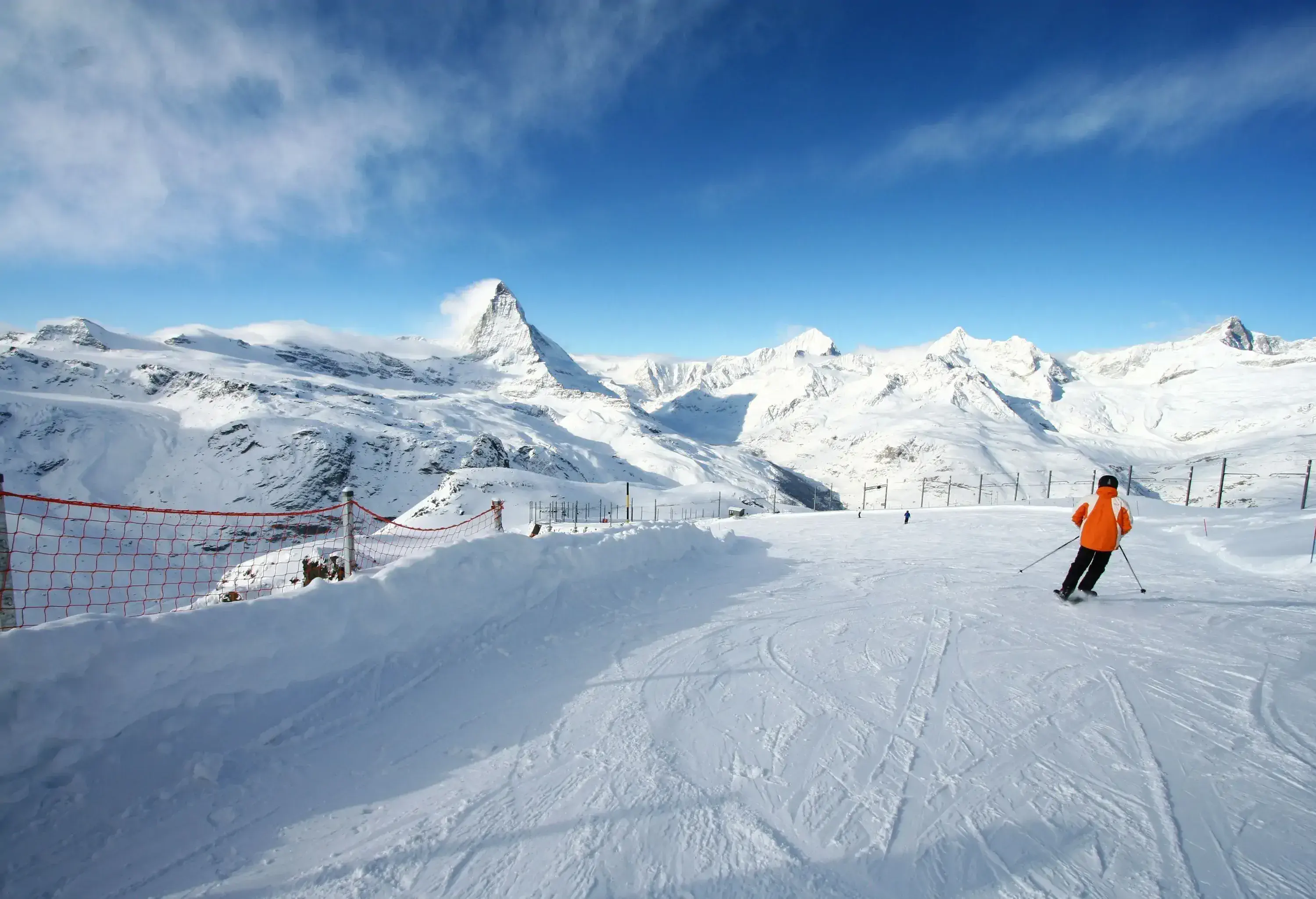 A skier smoothly gliding through a piste with a net perimeter fence.