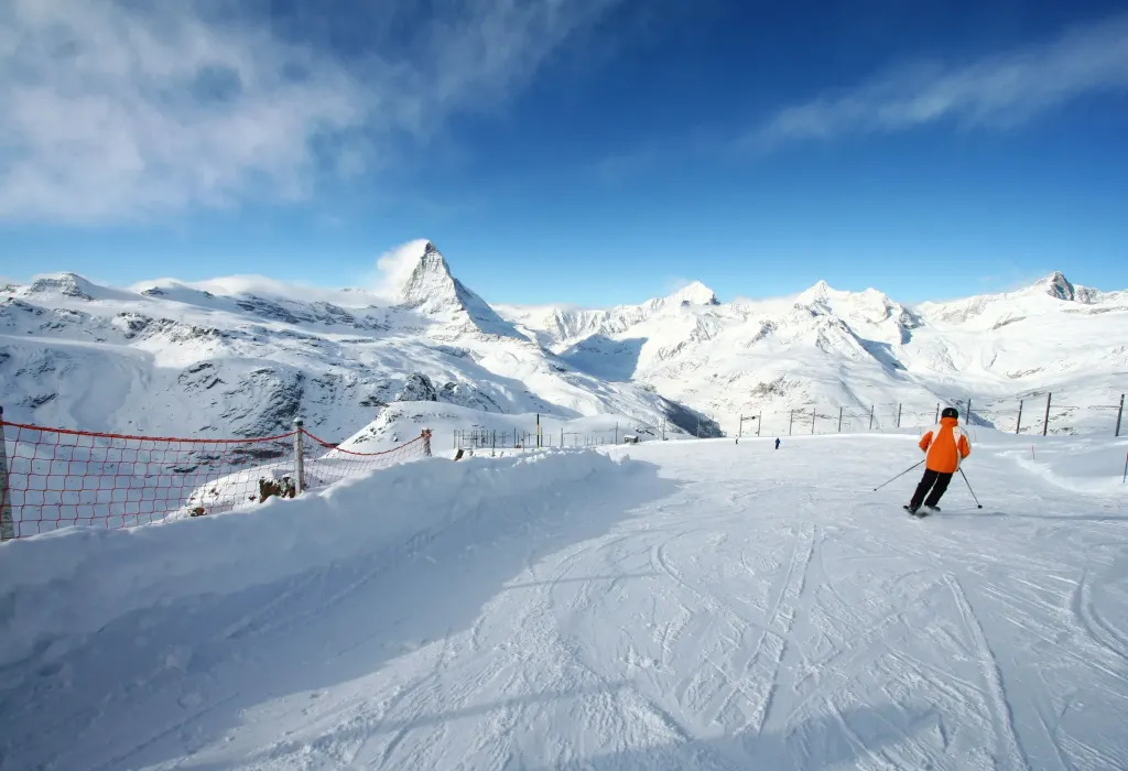 A skier smoothly gliding through a piste with a net perimeter fence.