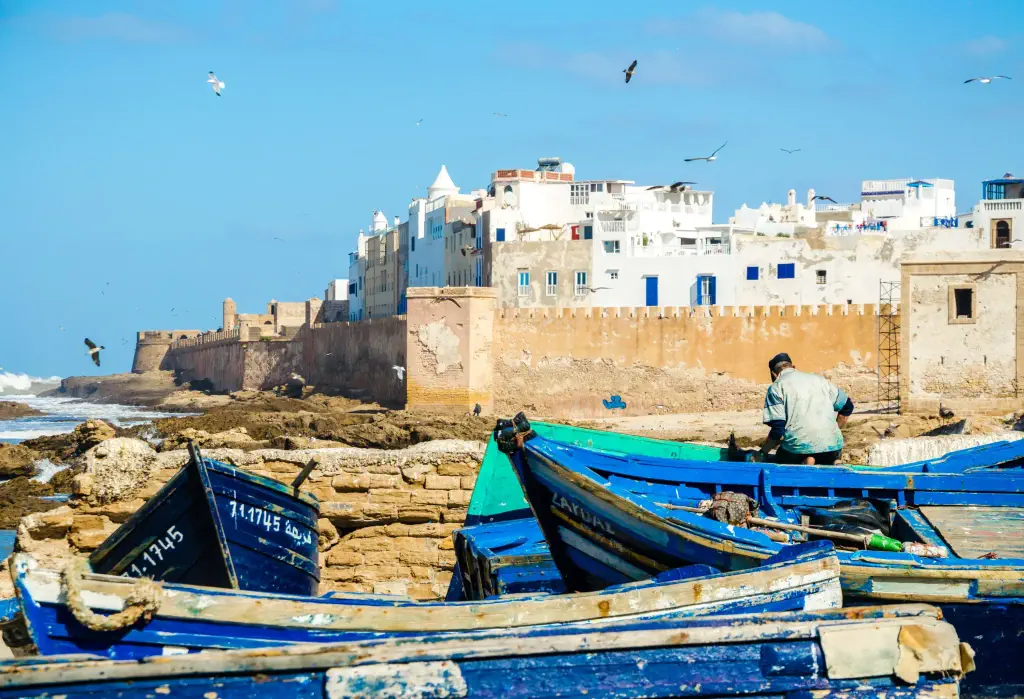 The blue boats of Essaouira are moored by the city's expansive coast, fringed by a beautiful sandy beach and protected by a magnificent stone wall.