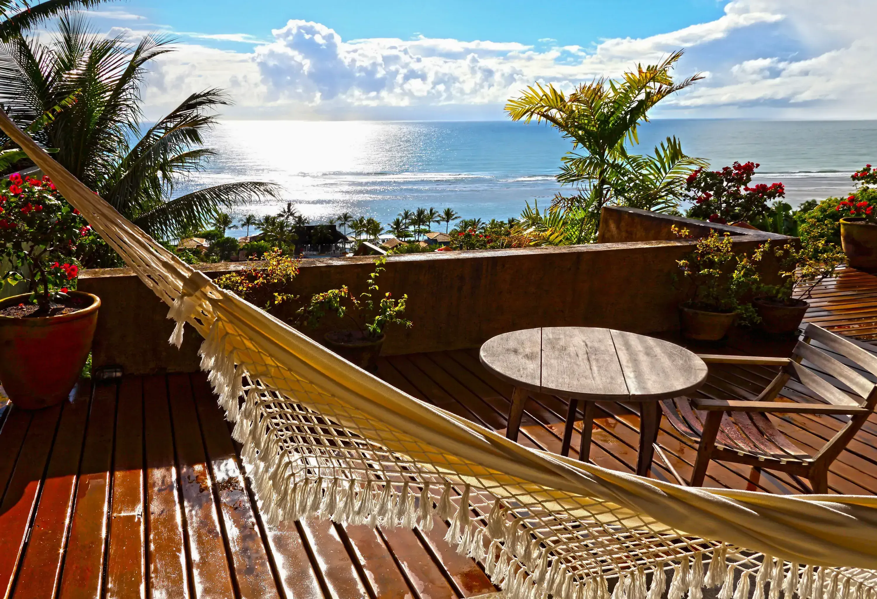 A balcony with outdoor seating area and hammock overlooking a vast ocean.