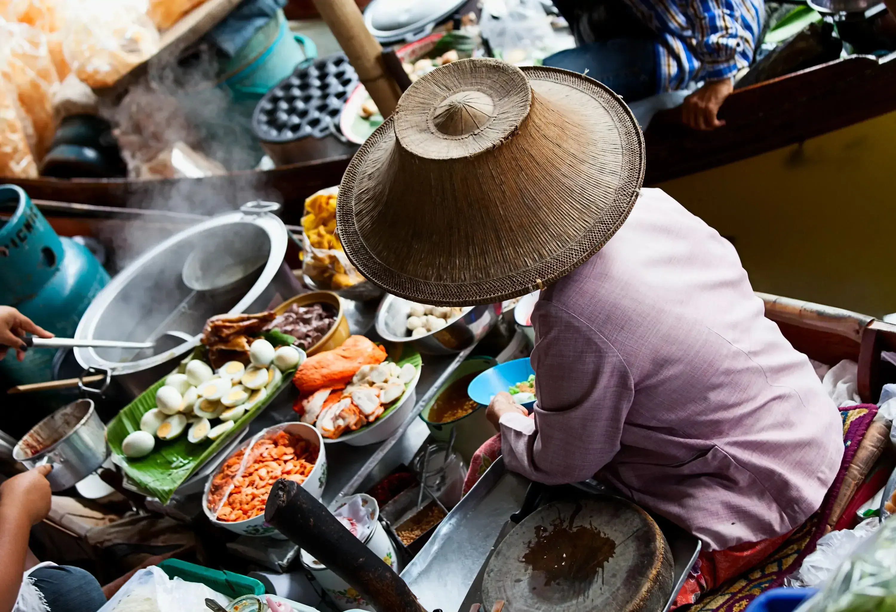 A vendor selling traditional food from a boat at a floating market.