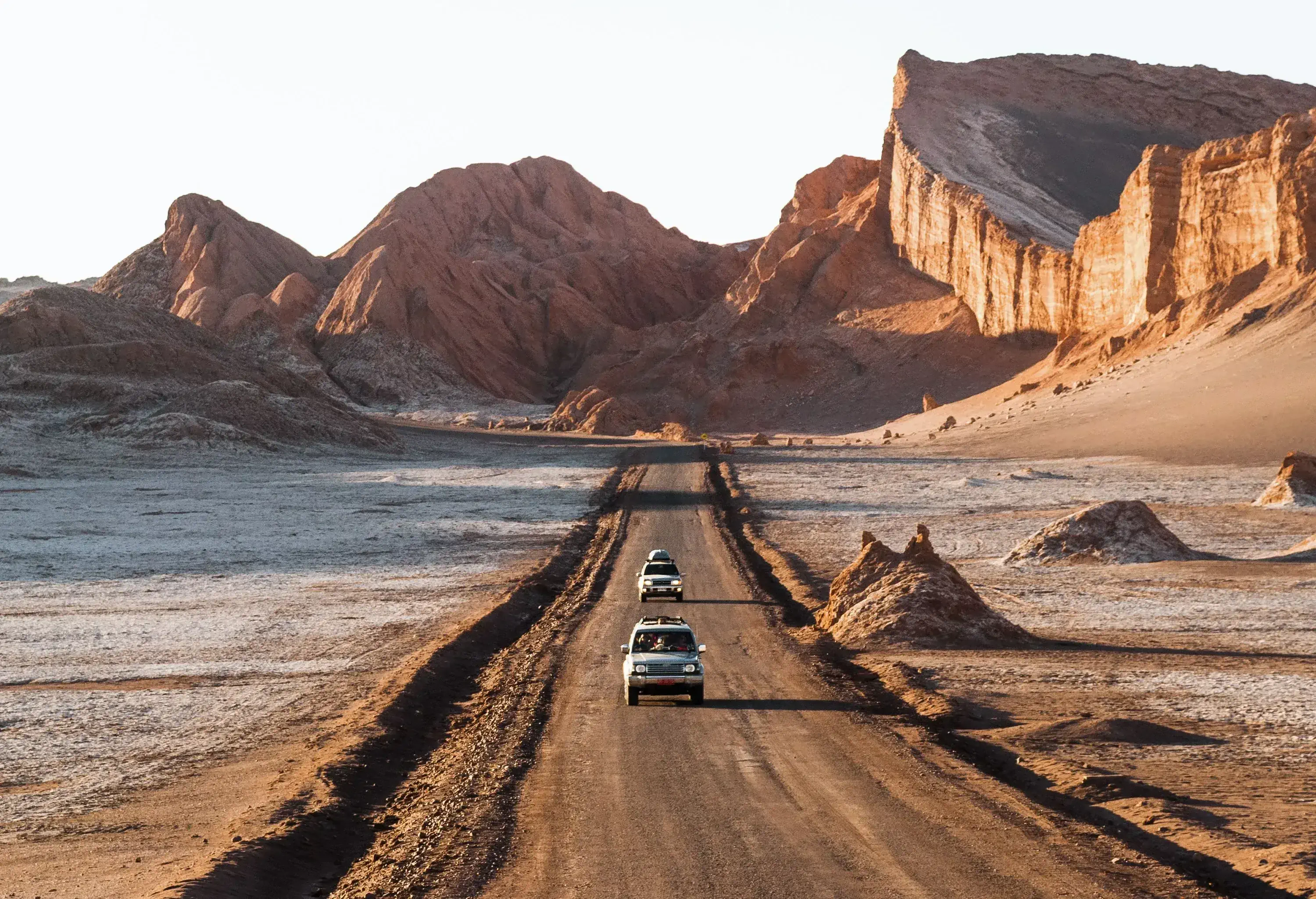Cars traverse a sandy road, surrounded by the rugged beauty of towering rock formations in the distance.